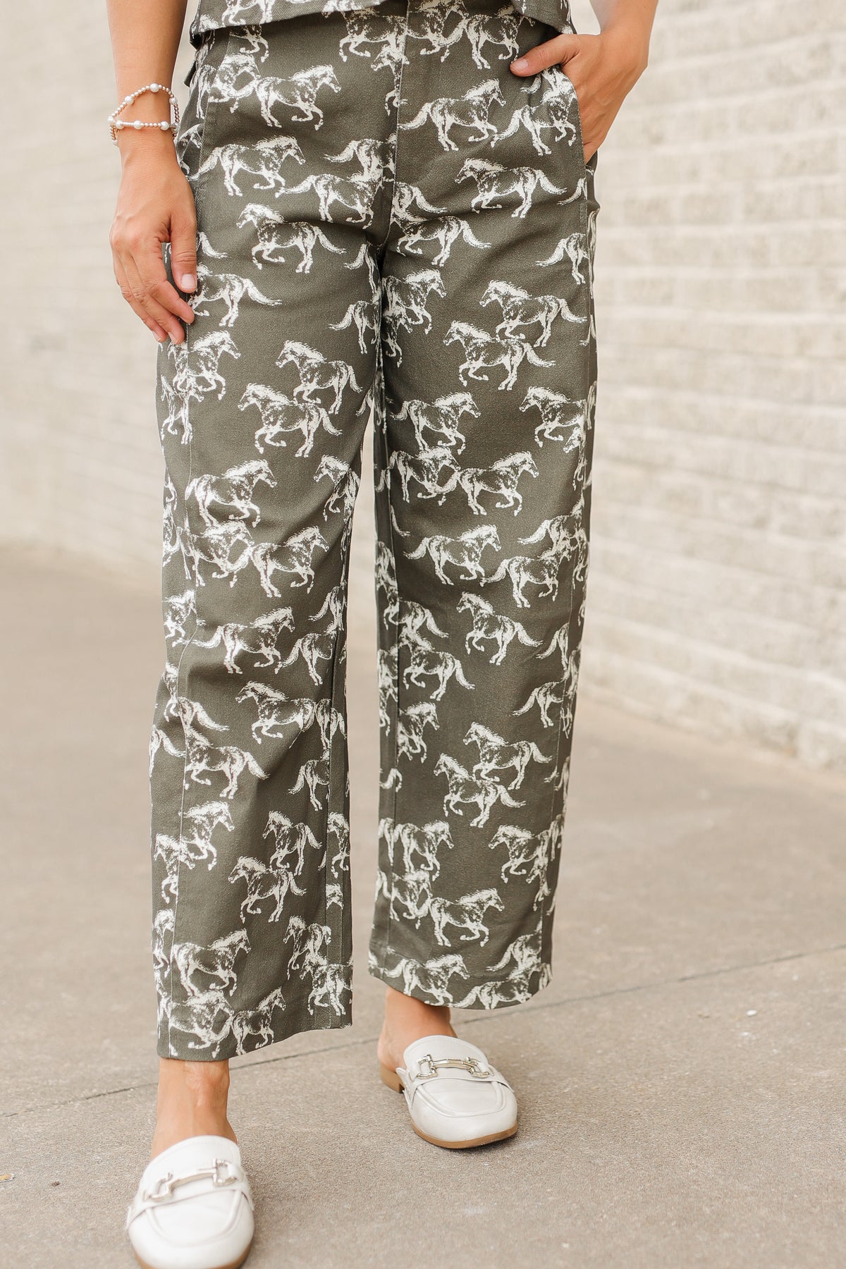 Brunette model wearing an olive colored denim set with running horse detail and white slides standing outside. Southern House Clothing.
