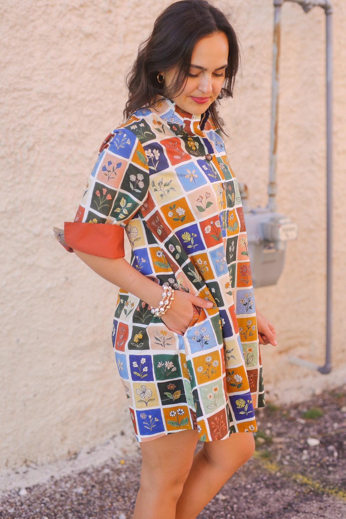 Woman wearing a colorful patterned dress against a beige wall.