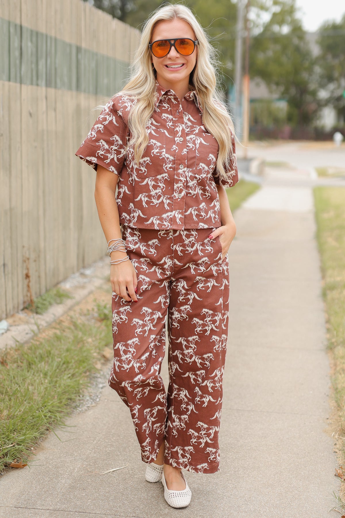 Blonde model wearing the Cibolo Running Horses Button-Up Top – Brown and matching denim bottoms - Cibolo Running Horses Wide Leg Pants – Brown standing outside. Southern House Clothing