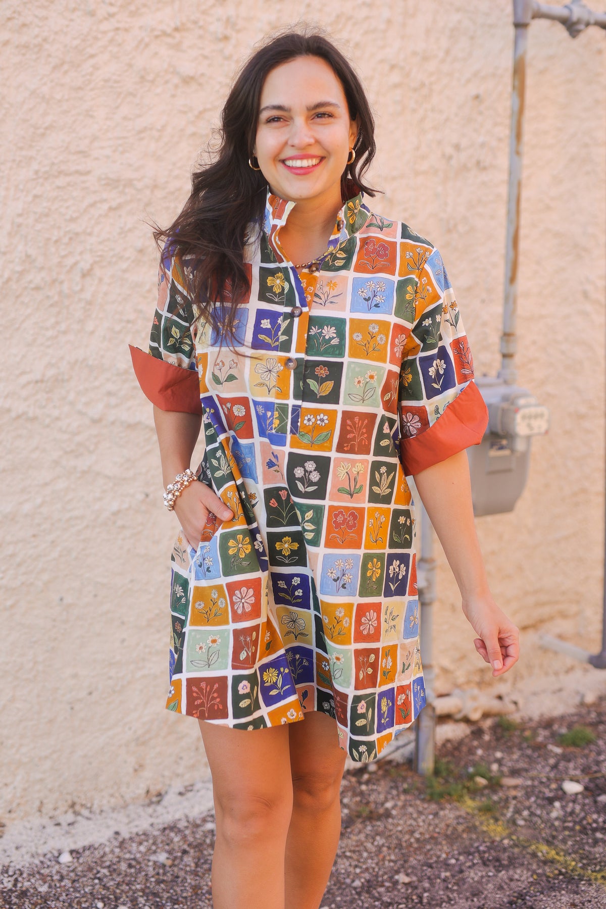 Woman wearing a colorful patterned dress standing against a beige wall.