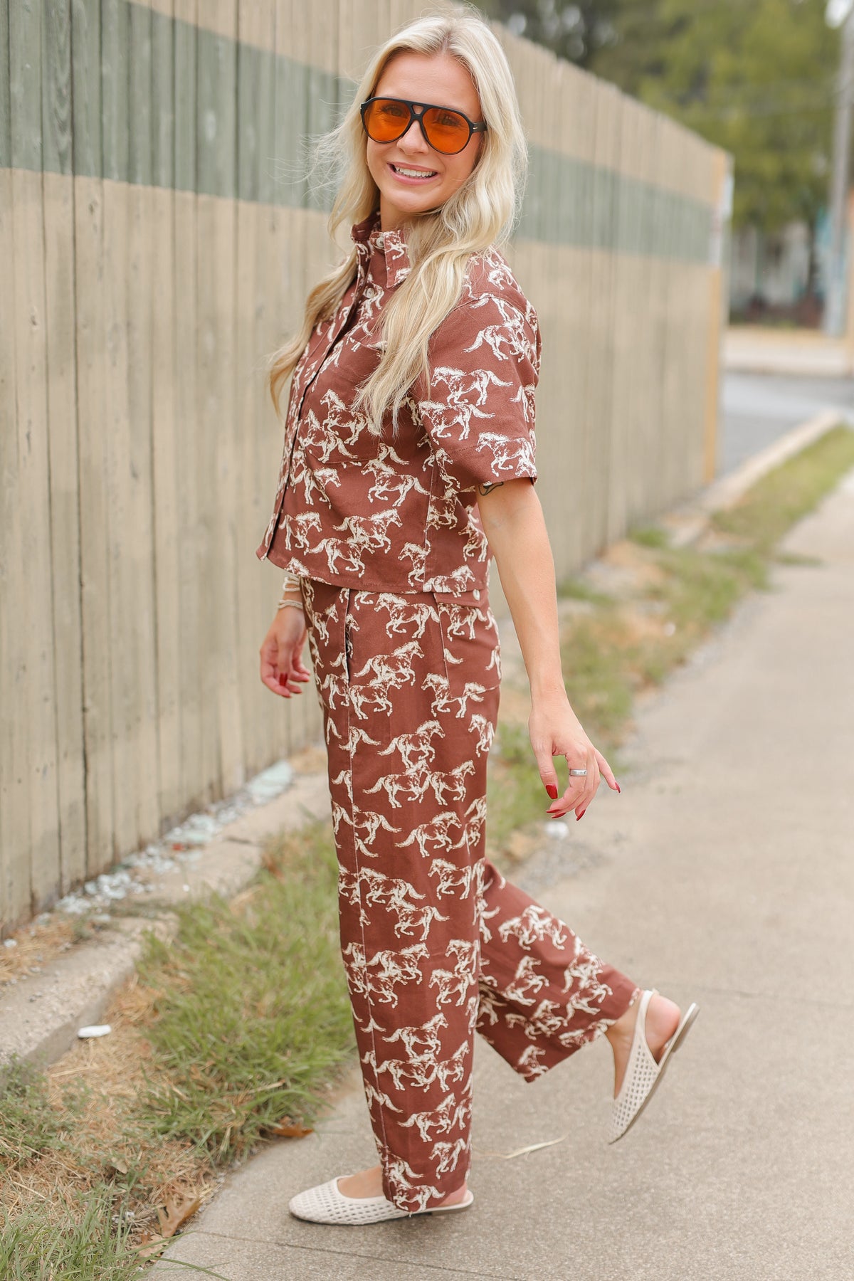 Blonde model wearing the Cibolo Running Horses Button-Up Top – Brown and matching denim bottoms - Cibolo Running Horses Wide Leg Pants – Brown standing outside. Southern House Clothing