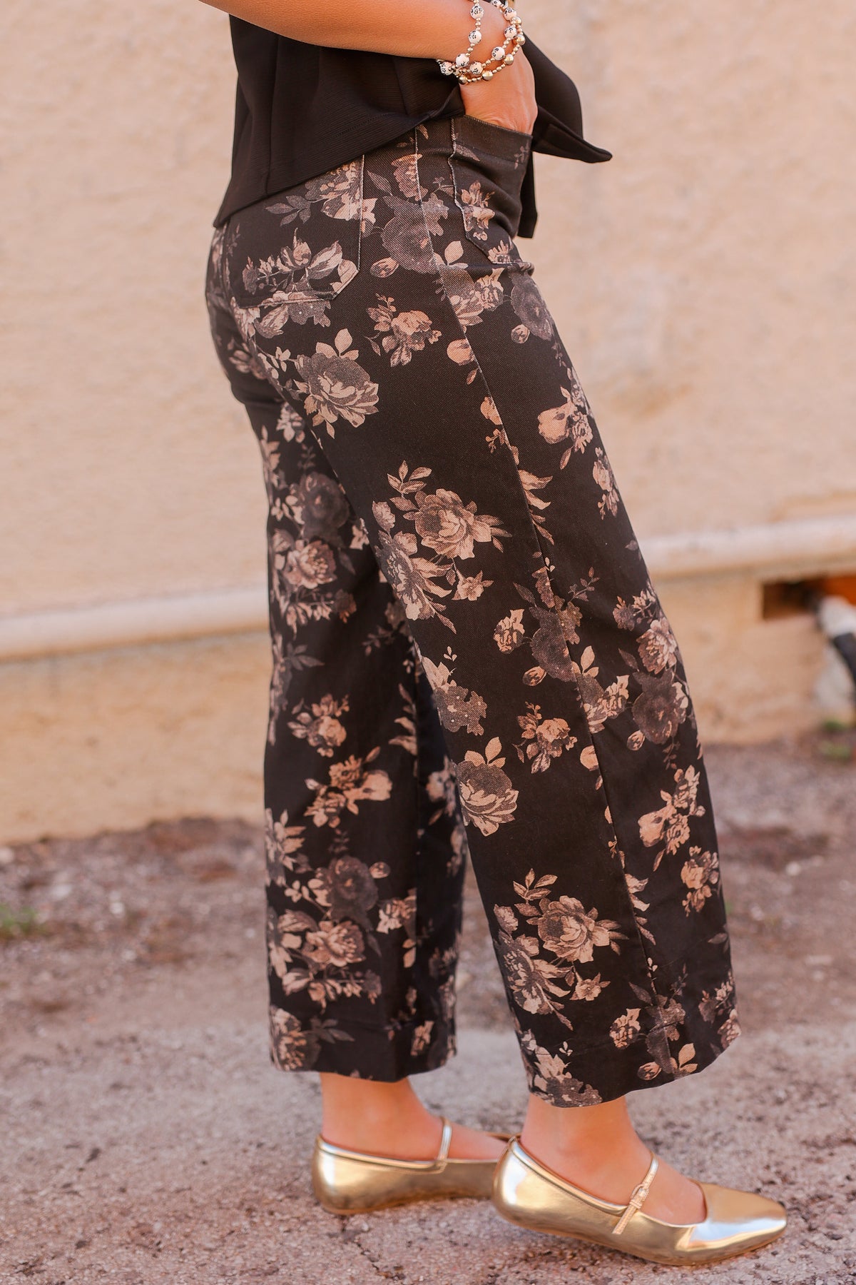 Person wearing black floral pants with gold shoes on a neutral background