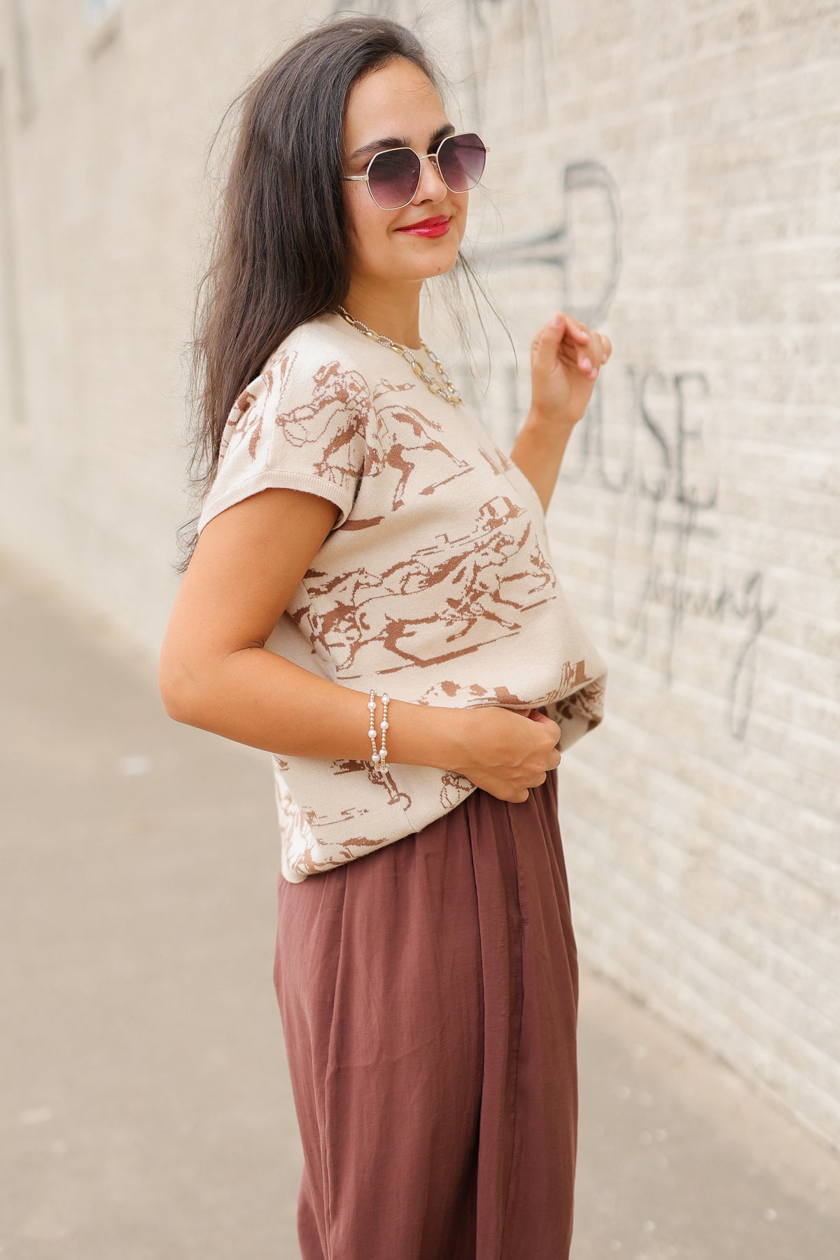 Model wearing Bronco Trail Knit Top in Ecru featuring taupe western cowboy, bucking horse, and desert cactus illustrations, styled with the Tulara Barrel Pants – Brown from Southern House Clothing.