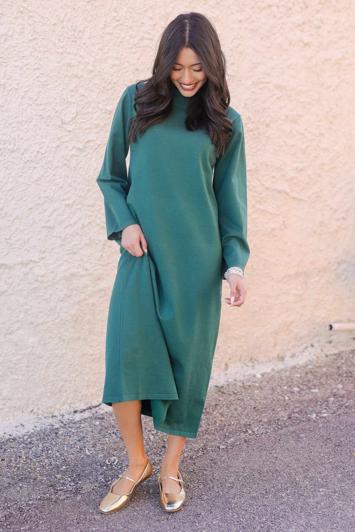 Woman wearing a green dress standing against a beige wall.