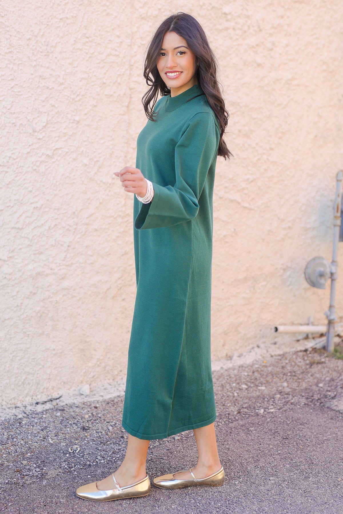Woman wearing a teal dress standing against a beige wall.