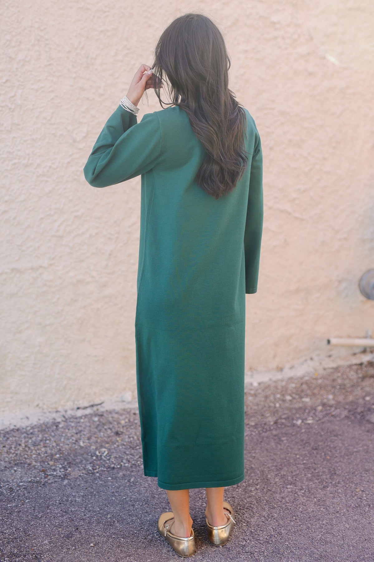 Person wearing a green dress standing against a beige wall.