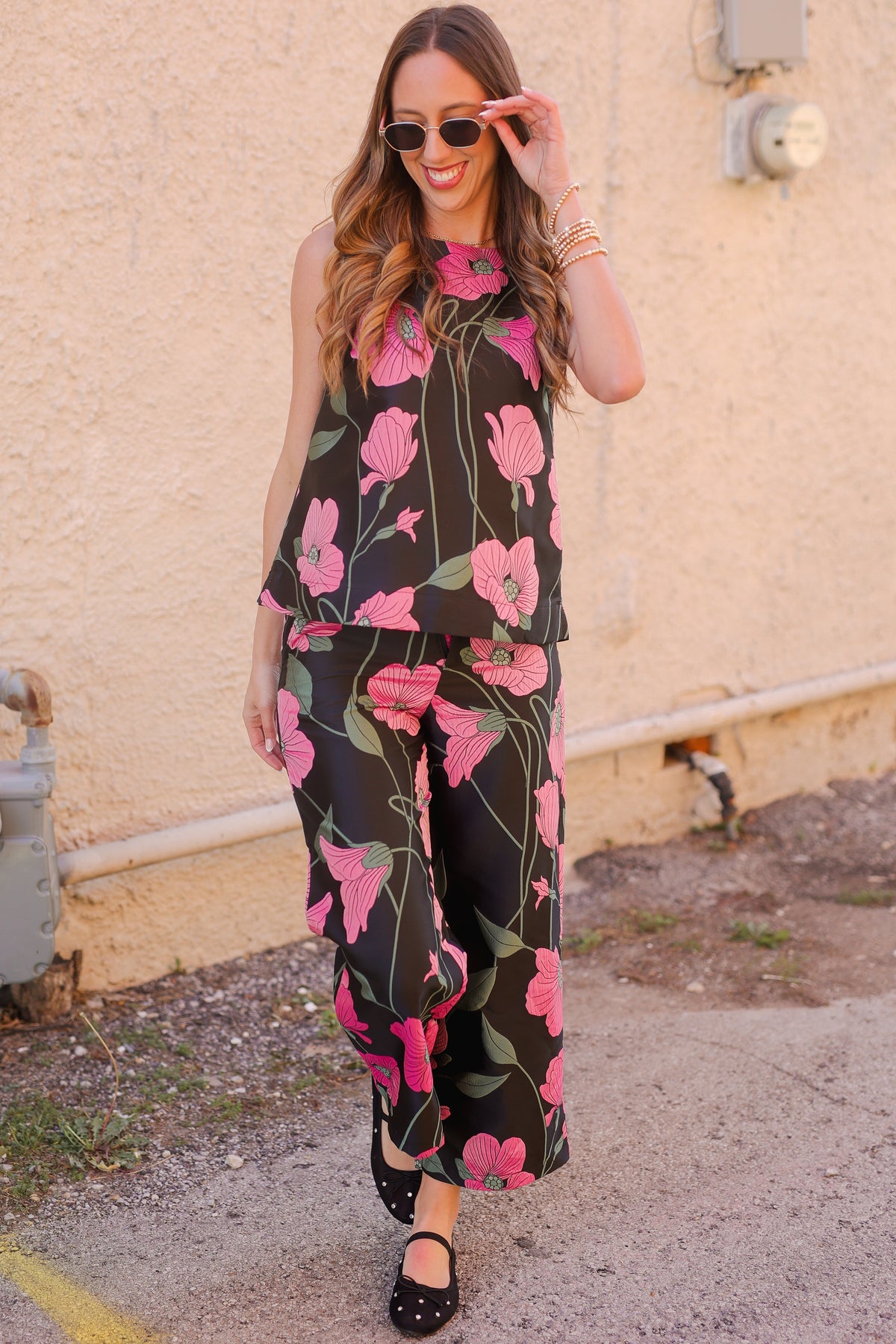 Woman wearing a black floral jumpsuit standing against a beige wall.