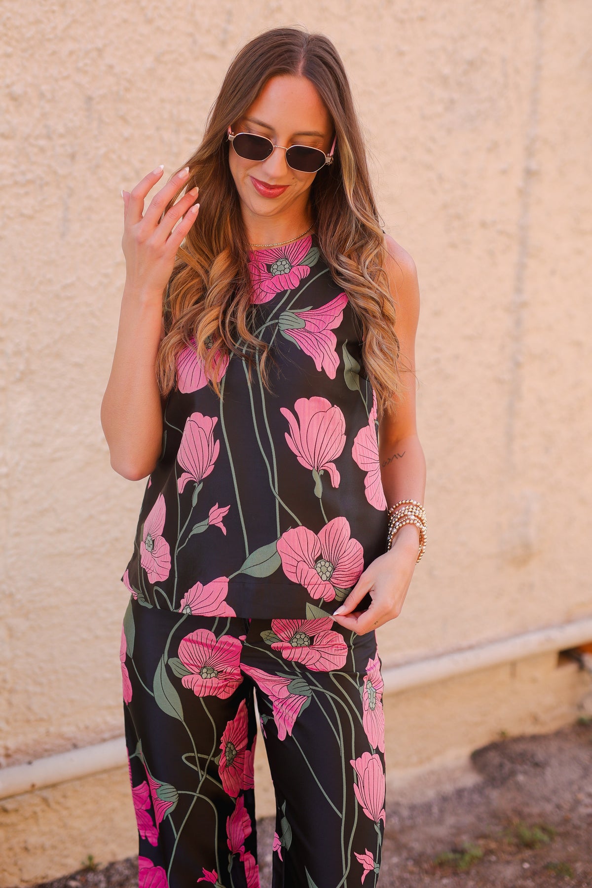 Woman wearing a black floral jumpsuit with pink flowers against a beige wall.