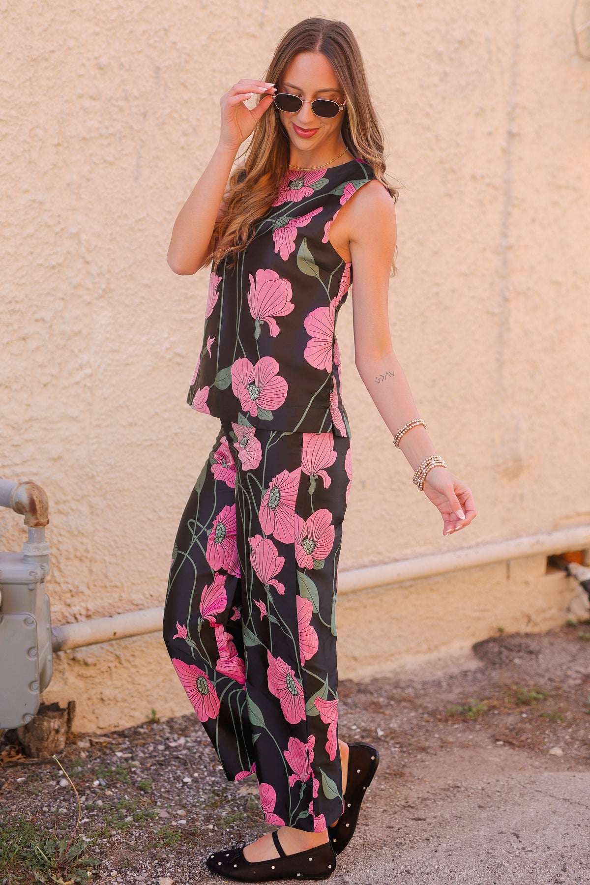 Woman wearing a black floral jumpsuit against a beige wall.