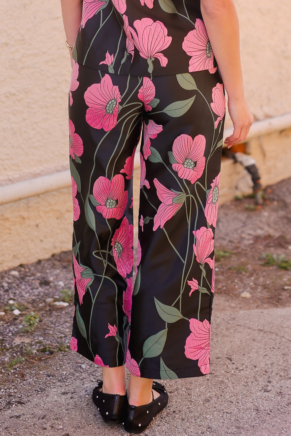 Person wearing a black jumpsuit with pink floral patterns on a concrete surface.