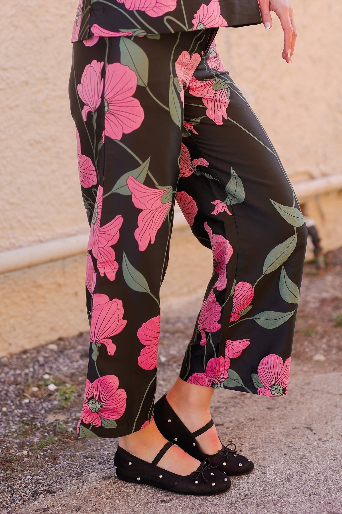 Floral-patterned pants with pink flowers on a black background, worn by a person.