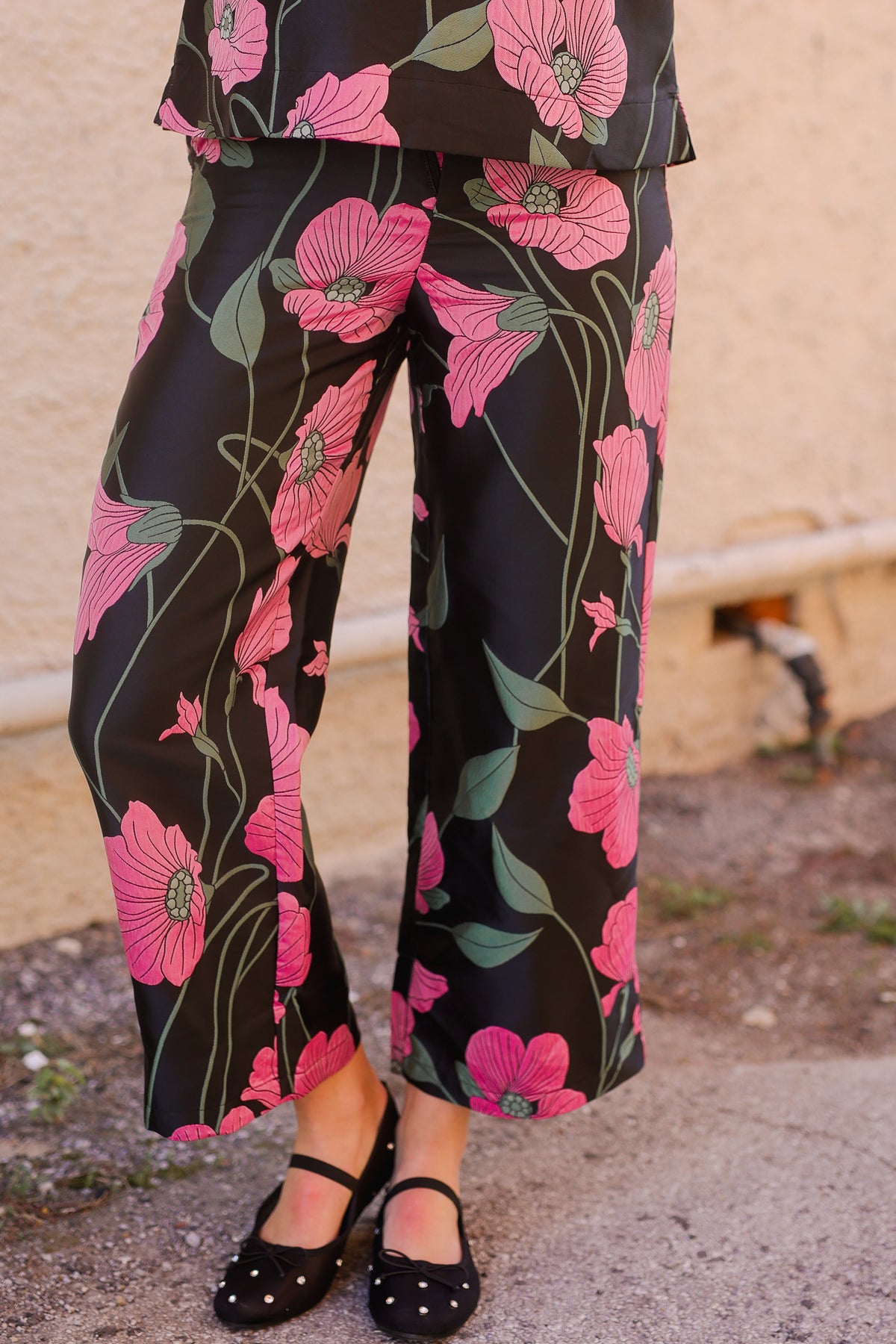 Floral pants with pink flowers on a black background worn by a person.
