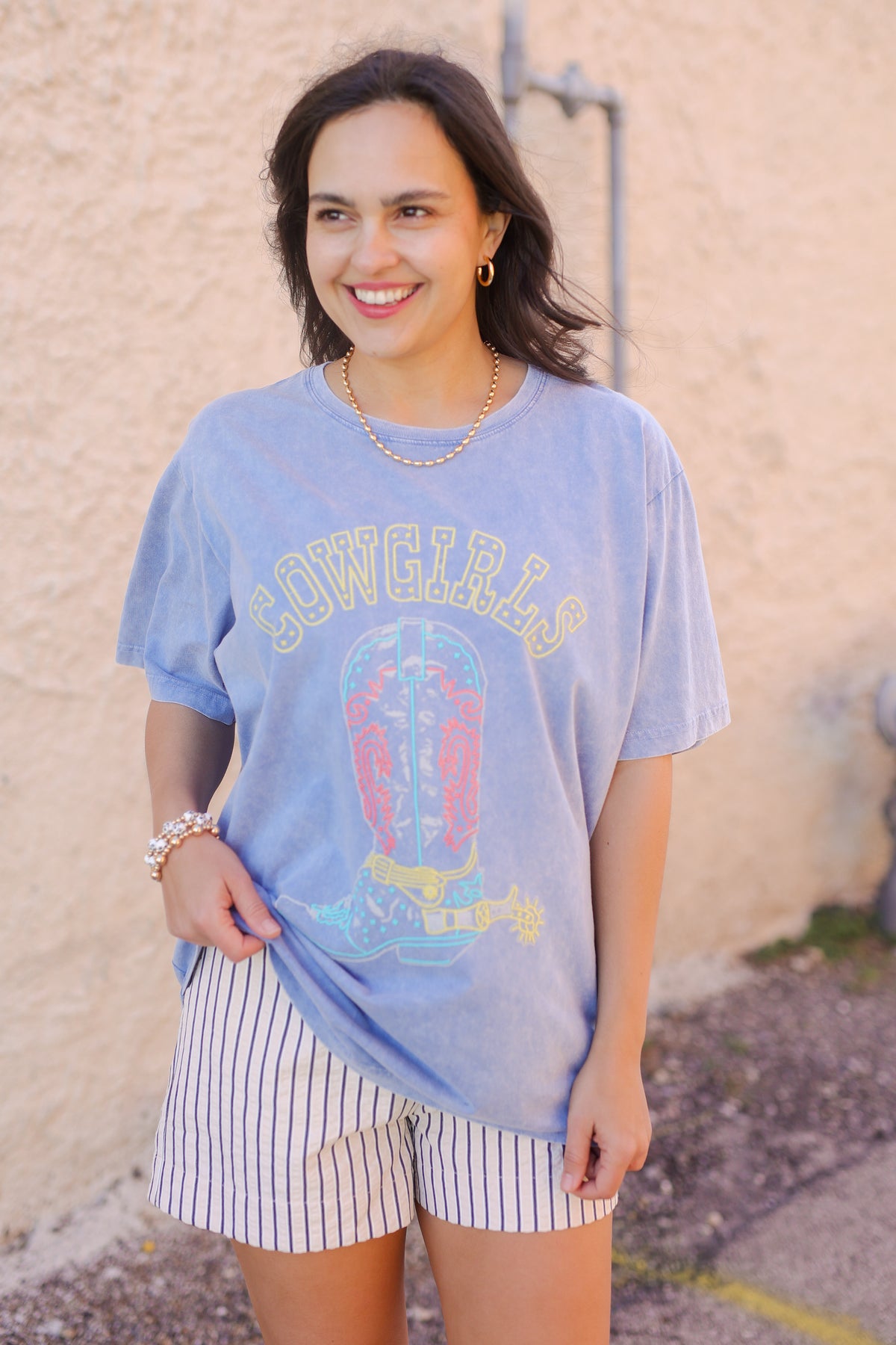 Woman wearing a blue graphic t-shirt and striped shorts against a beige wall.