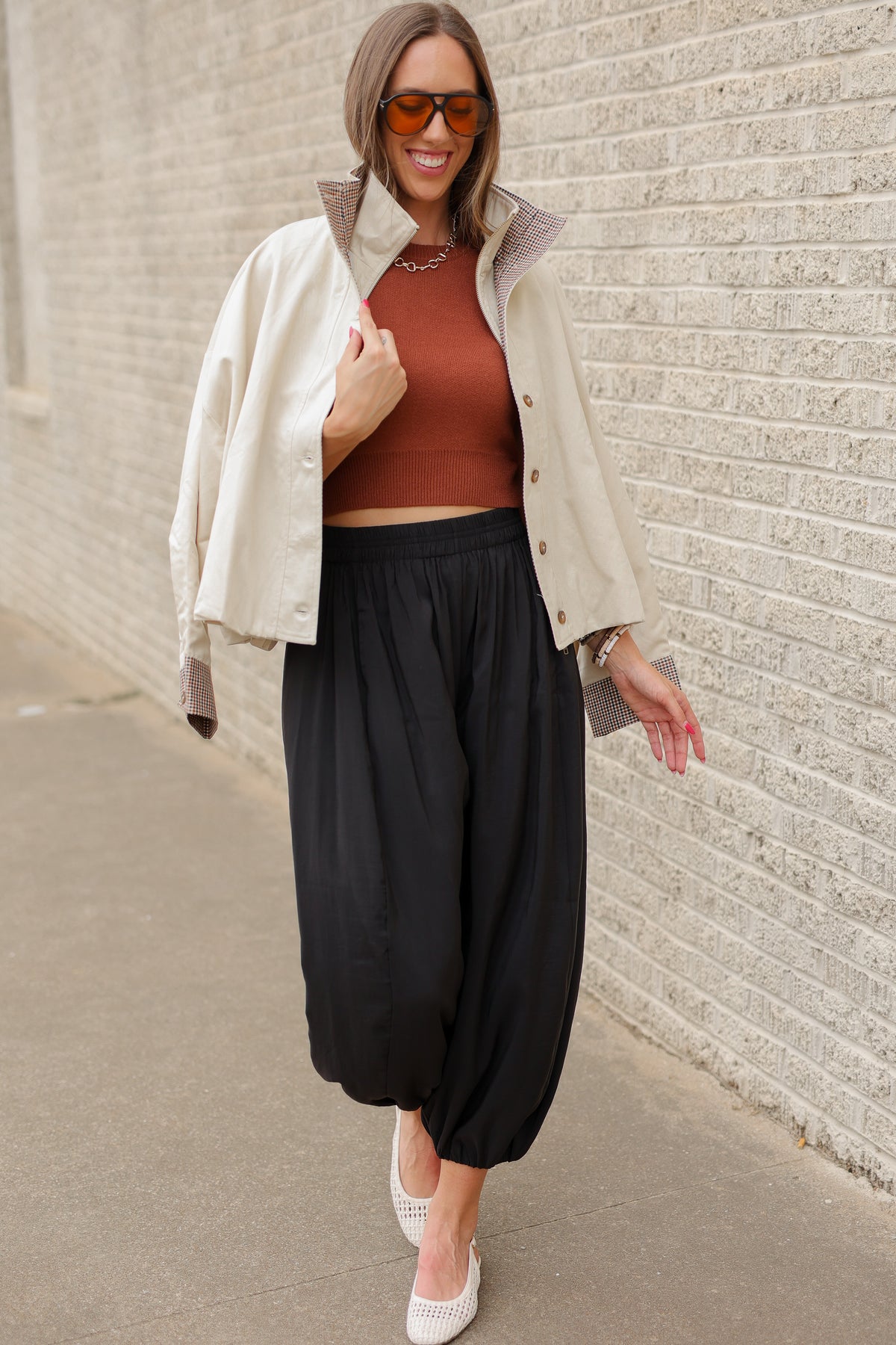 Blonde model wearing an ivory multi jacket, cinnamon colored tank and black pants standing outside. Southern House Clothing