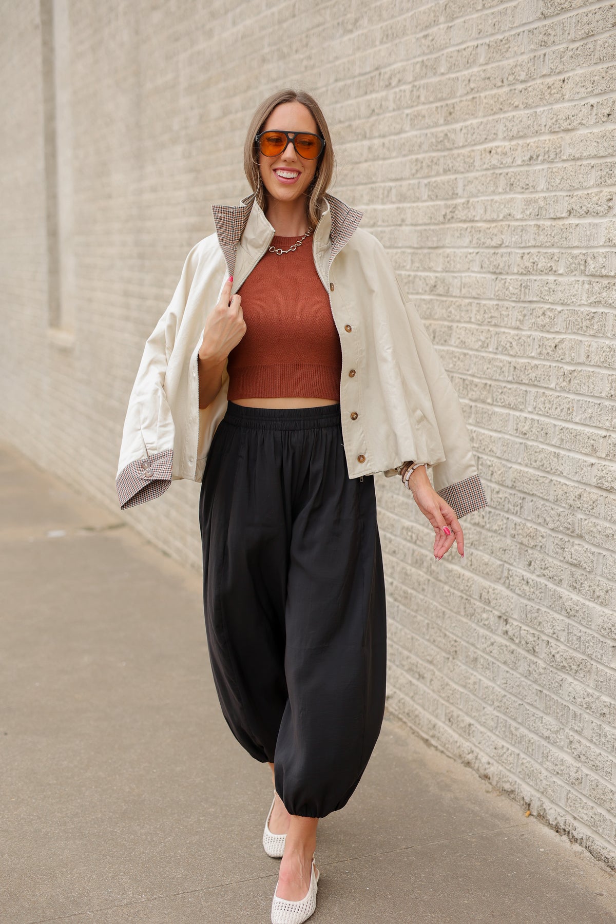 Blonde model wearing an ivory multi jacket, cinnamon colored tank and black pants standing outside. Southern House Clothing