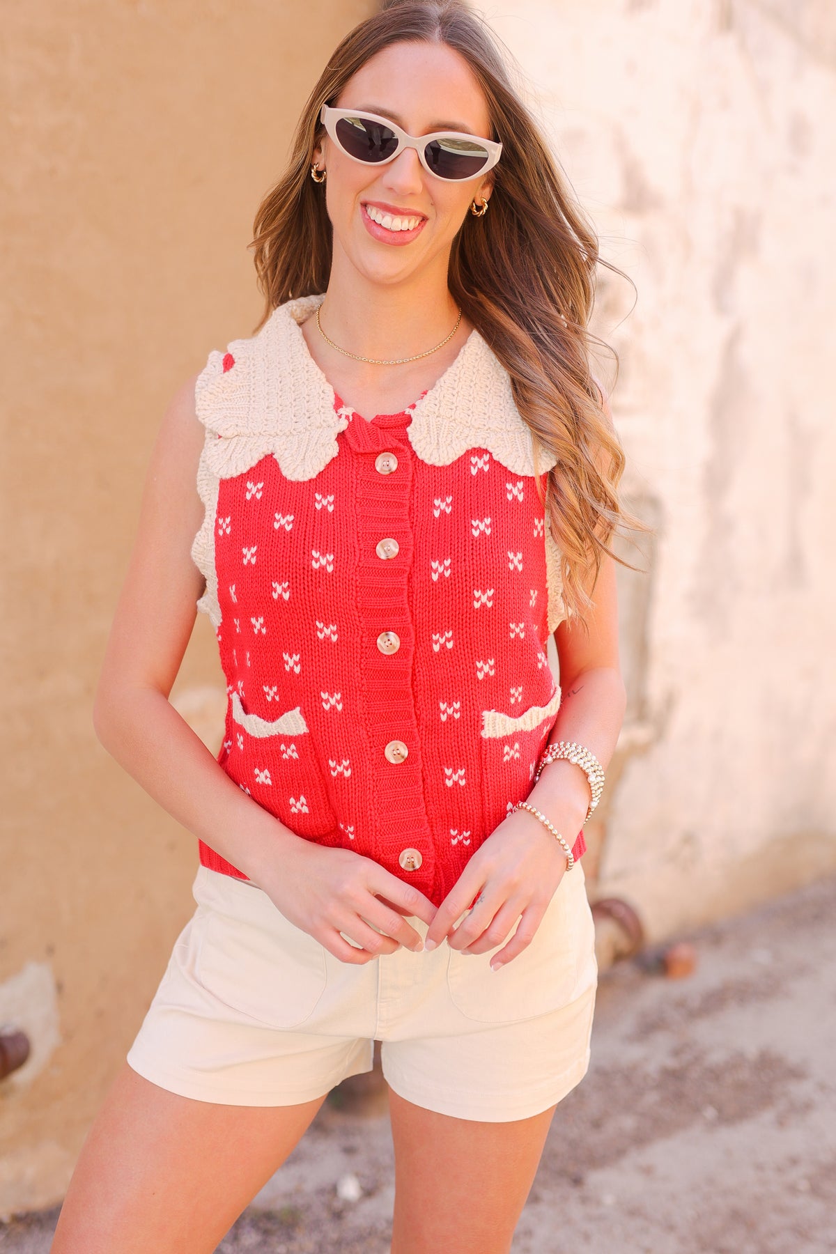 Woman wearing a red patterned top and white shorts with sunglasses outdoors.