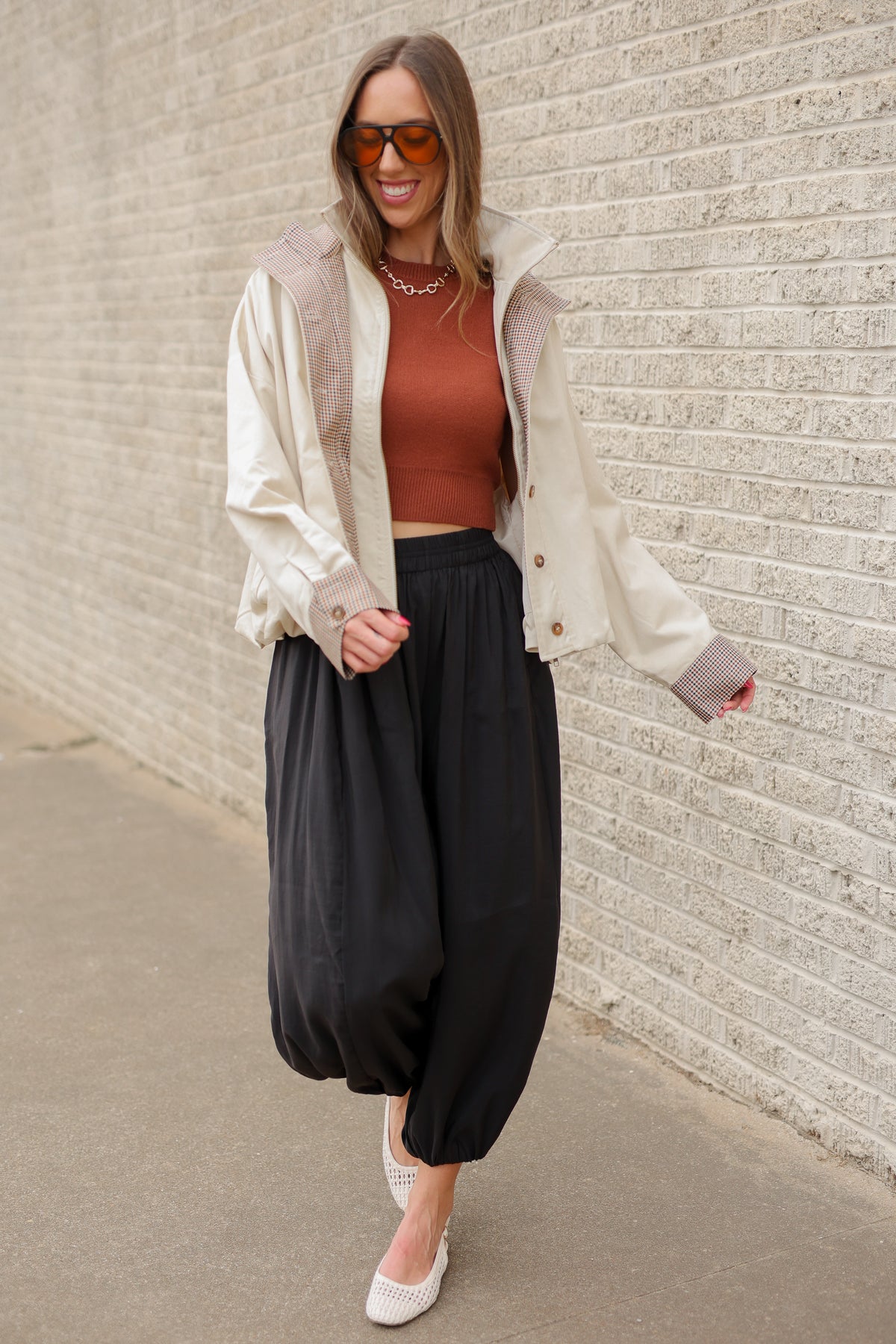 Blonde model wearing an ivory multi jacket, cinnamon colored tank and black pants standing outside. Southern House Clothing