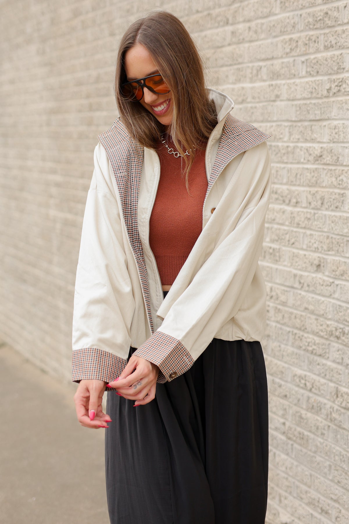 Blonde model wearing an ivory multi jacket, cinnamon colored tank and black pants standing outside. Southern House Clothing