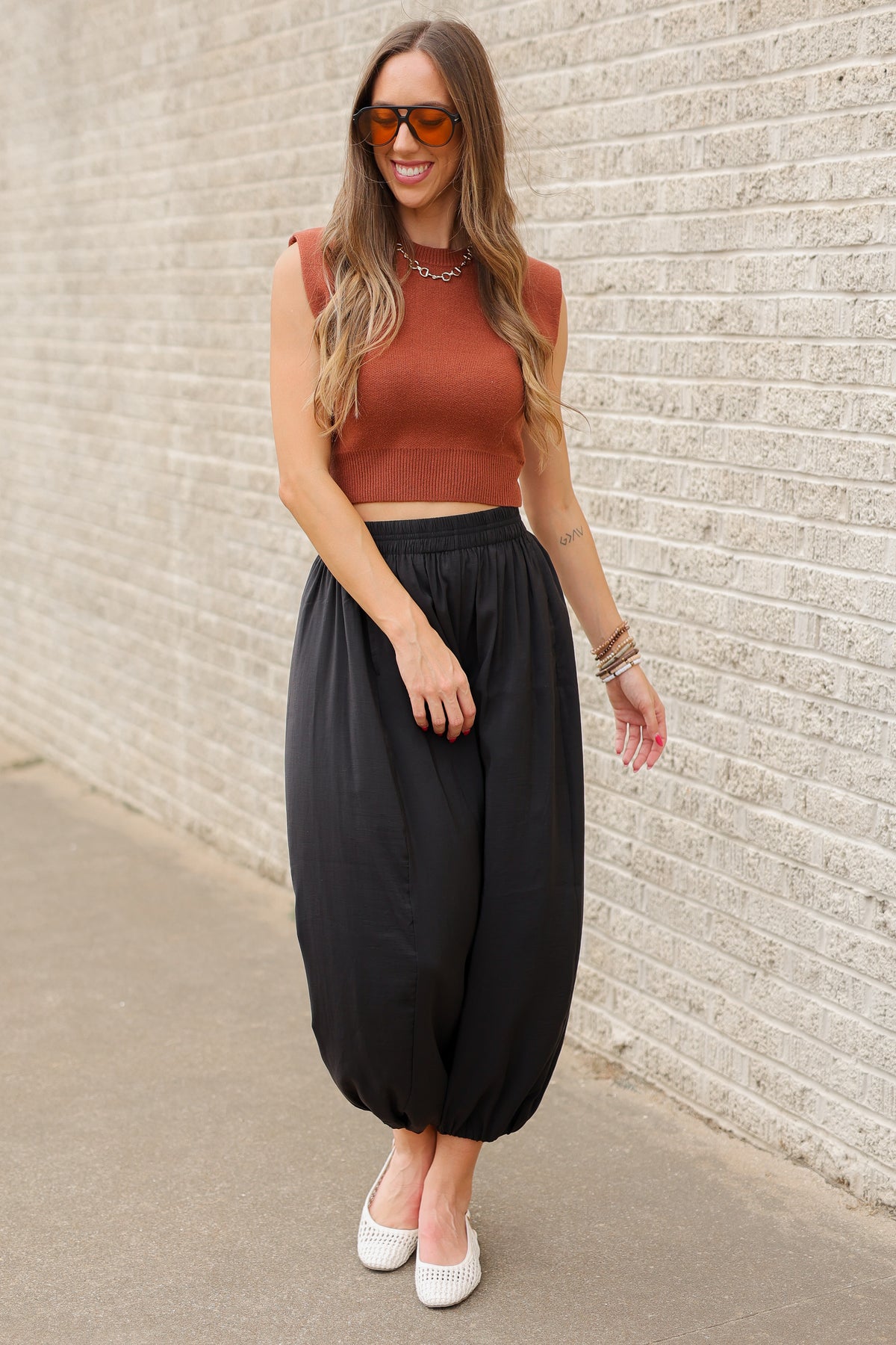 Blonde model wearing a cinnamon colored tank and black pants standing outside. Southern House Clothing