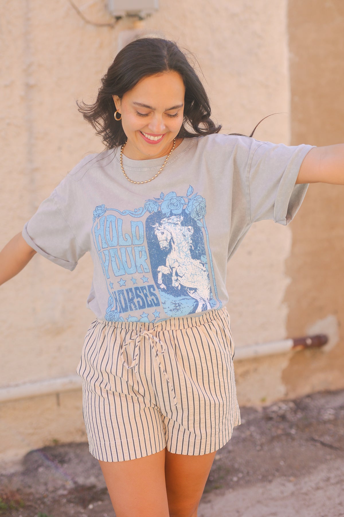 Woman wearing a graphic t-shirt and shorts standing in front of a beige wall.