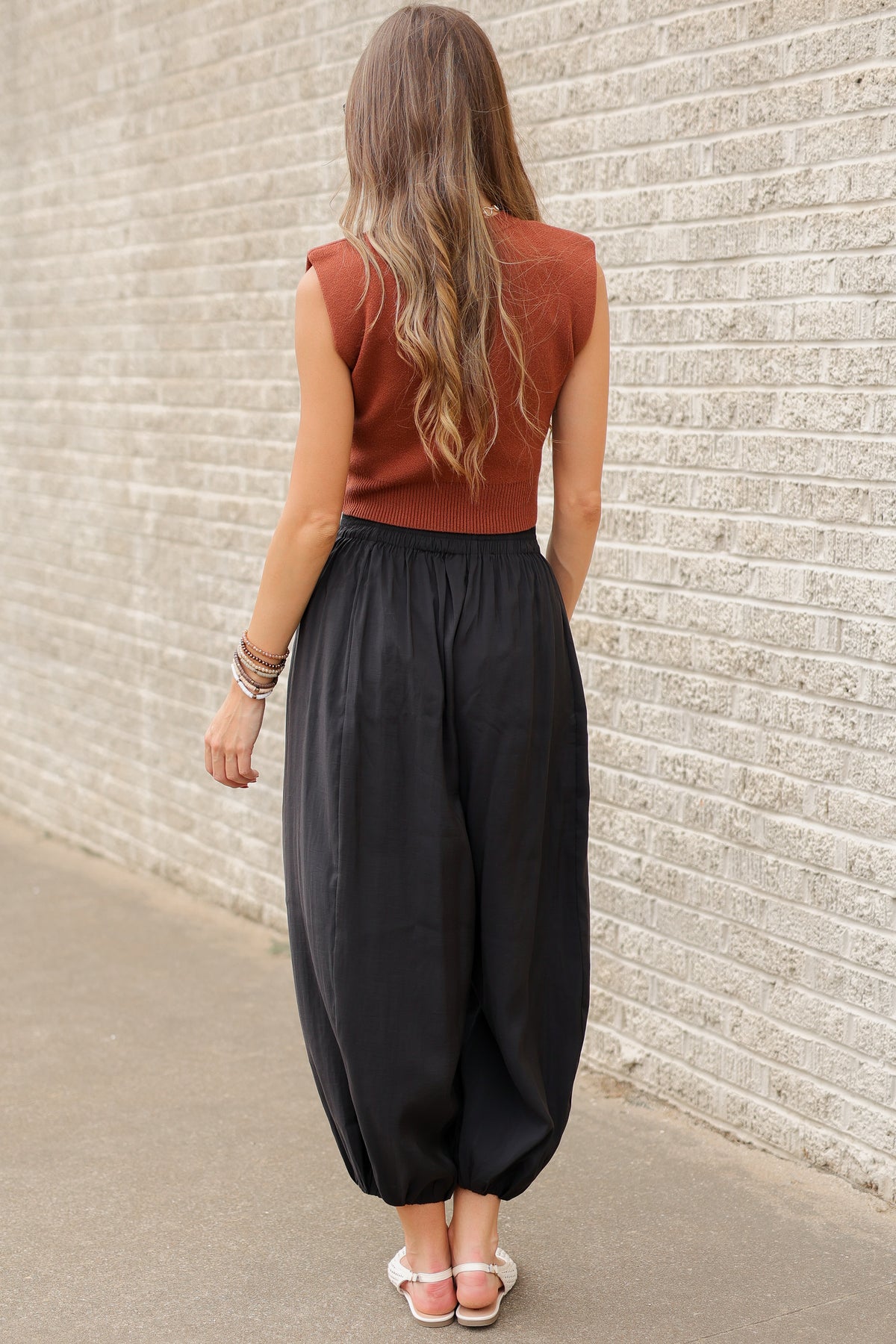 Blonde model wearing a cinnamon colored tank and black pants standing outside. Southern House Clothing