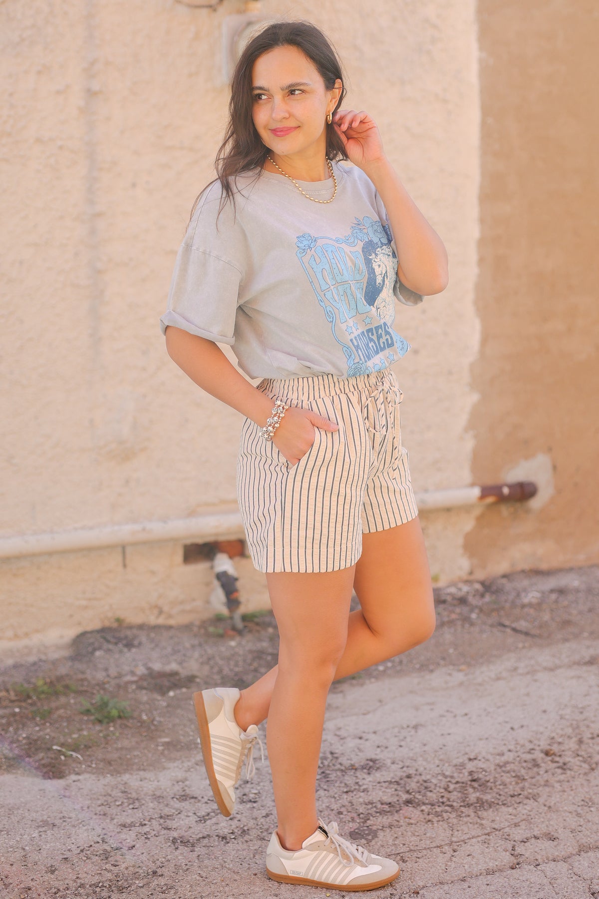 Woman wearing a graphic t-shirt and striped shorts standing against a beige wall.
