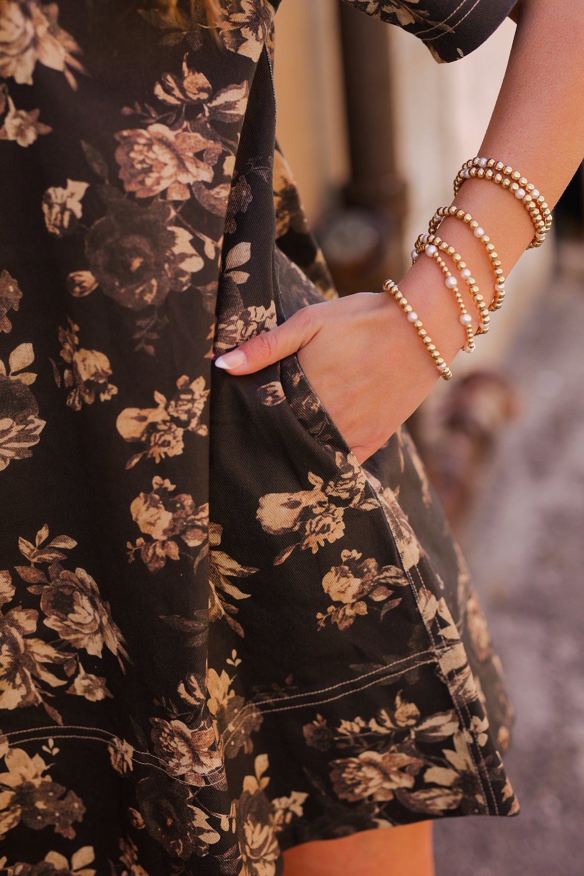 Close-up of a person wearing a black floral dress with gold accents and multiple bracelets.
