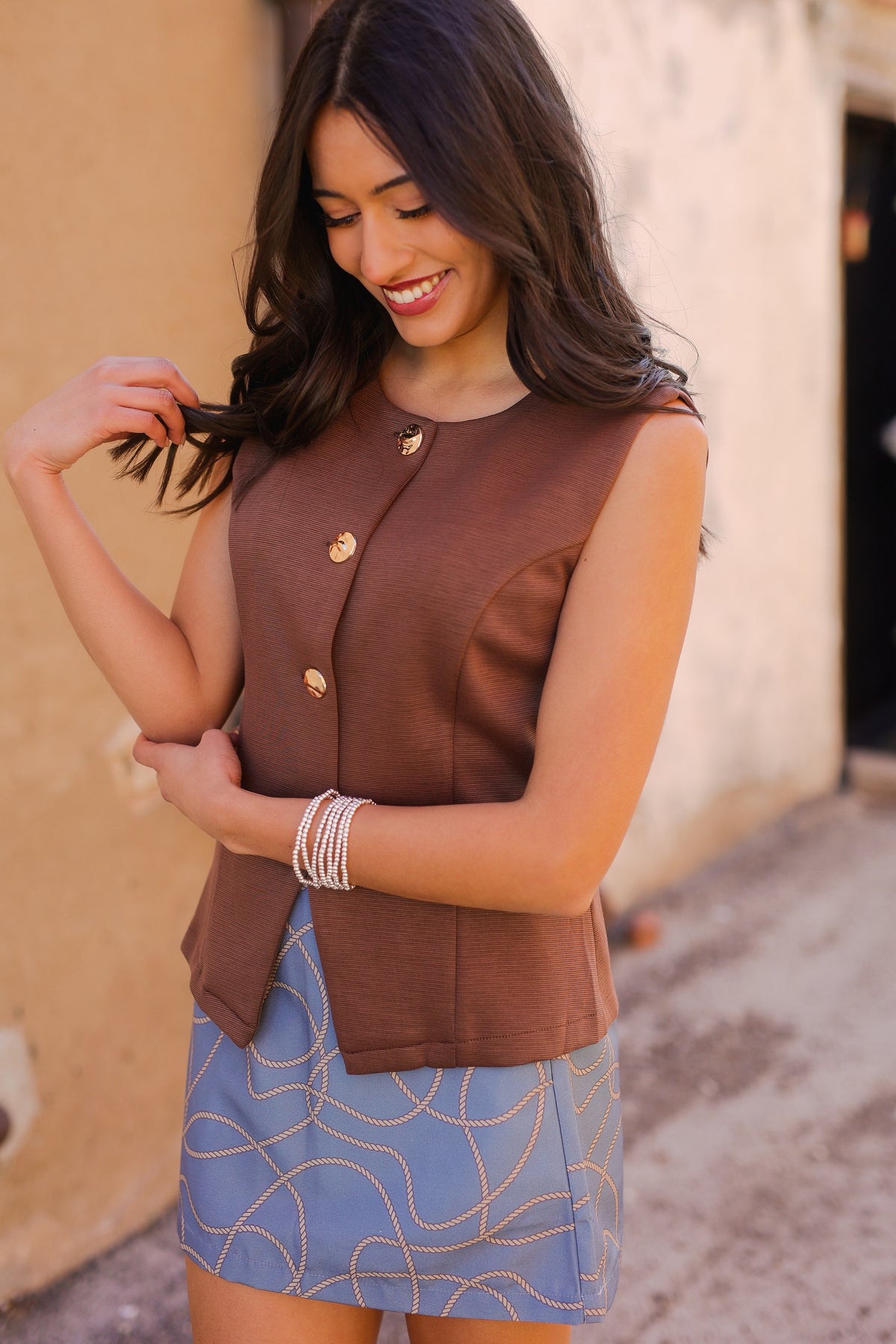 Woman wearing a brown sleeveless top and blue skirt with a beige wall background