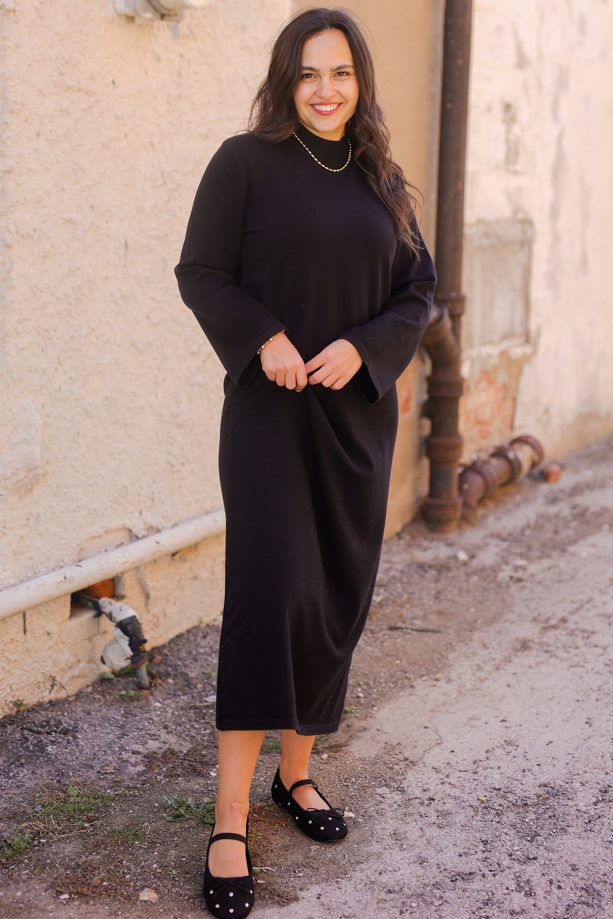 Woman wearing a black outfit standing against a textured wall.
