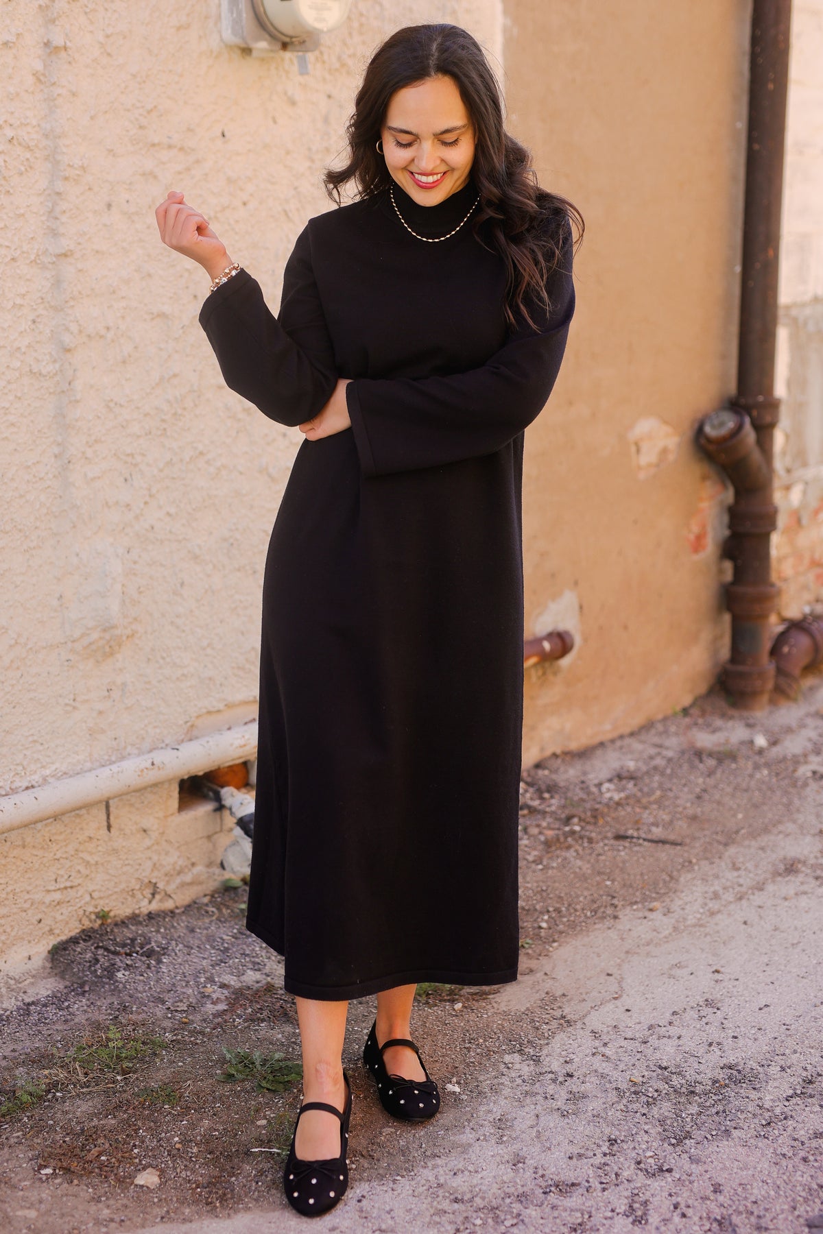 Woman wearing a black dress standing against a beige wall.