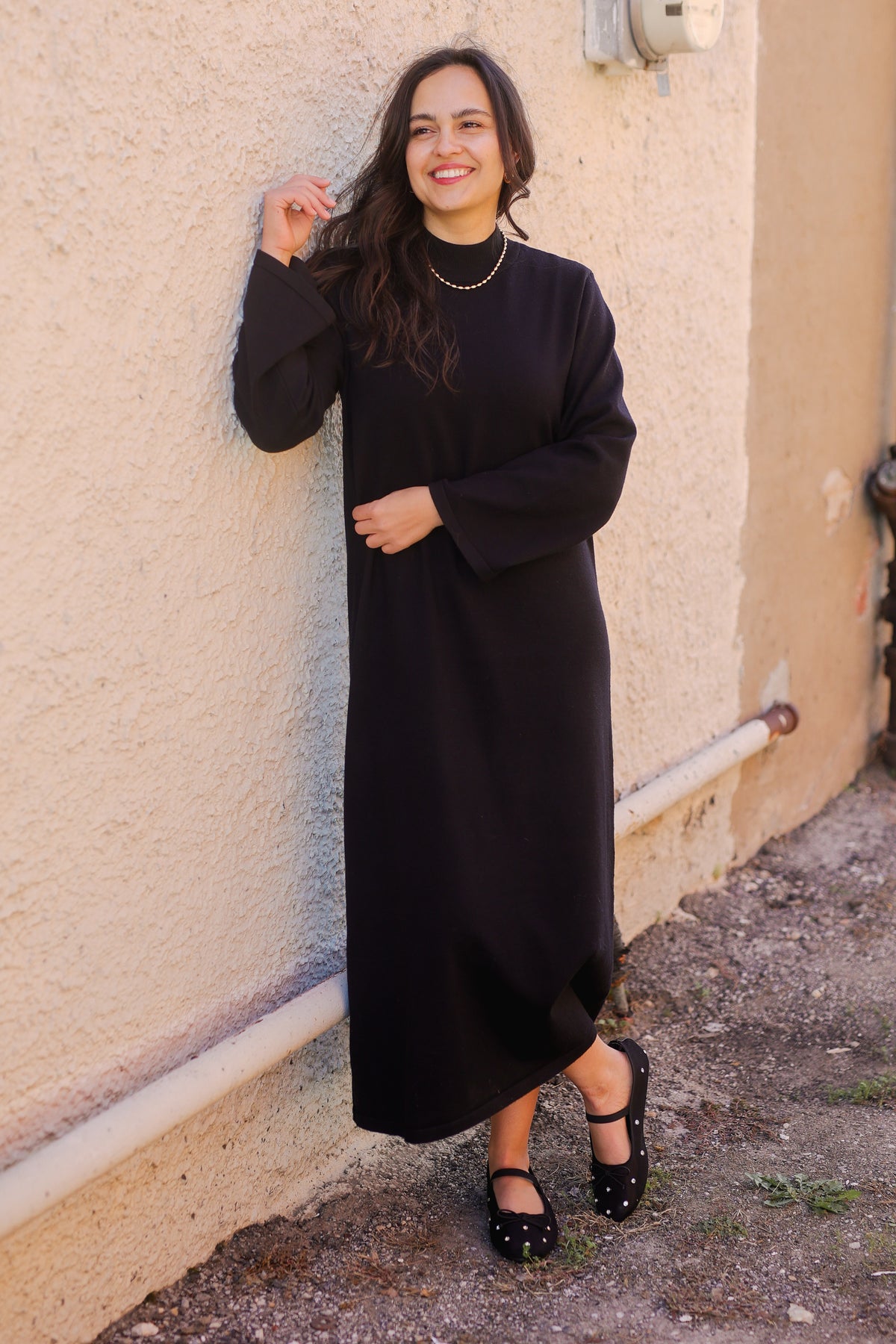 Woman wearing a black dress standing against a beige wall.
