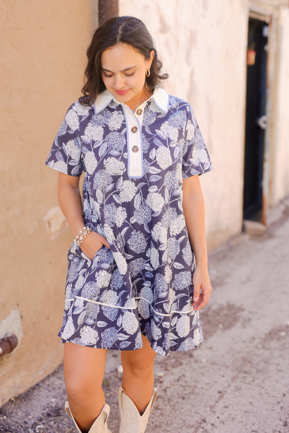 Woman wearing a blue floral dress with a white collar in an outdoor setting.