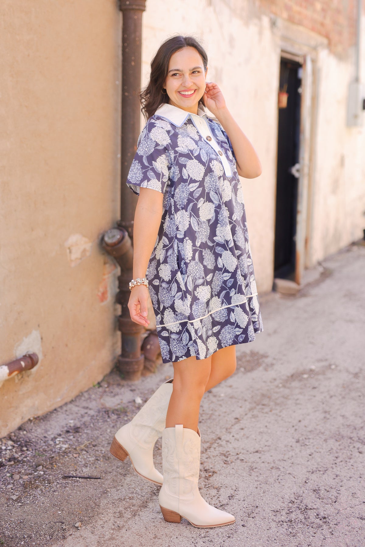 Woman in a floral dress and white boots standing on a street.