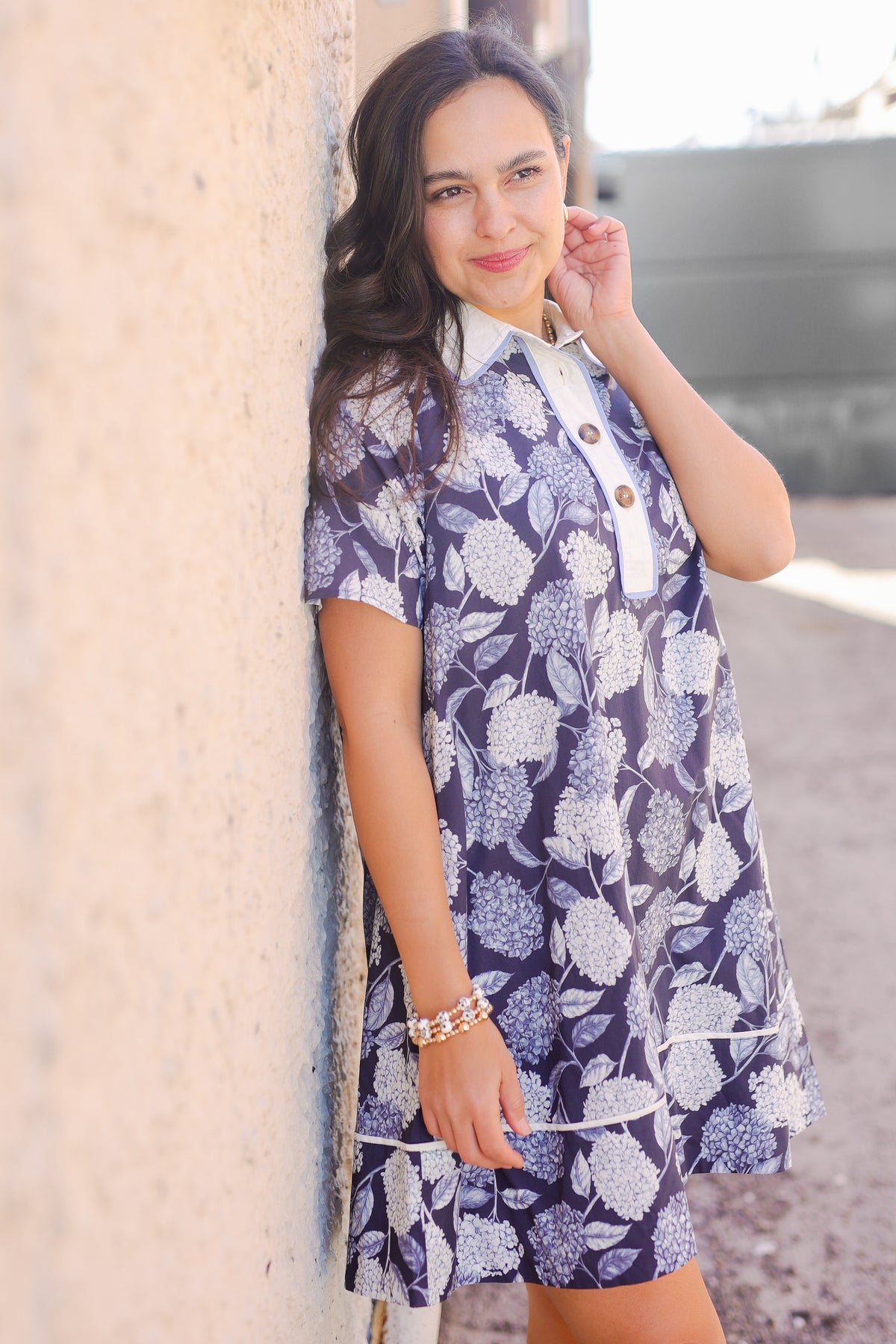 Woman wearing a blue floral dress leaning against a wall.