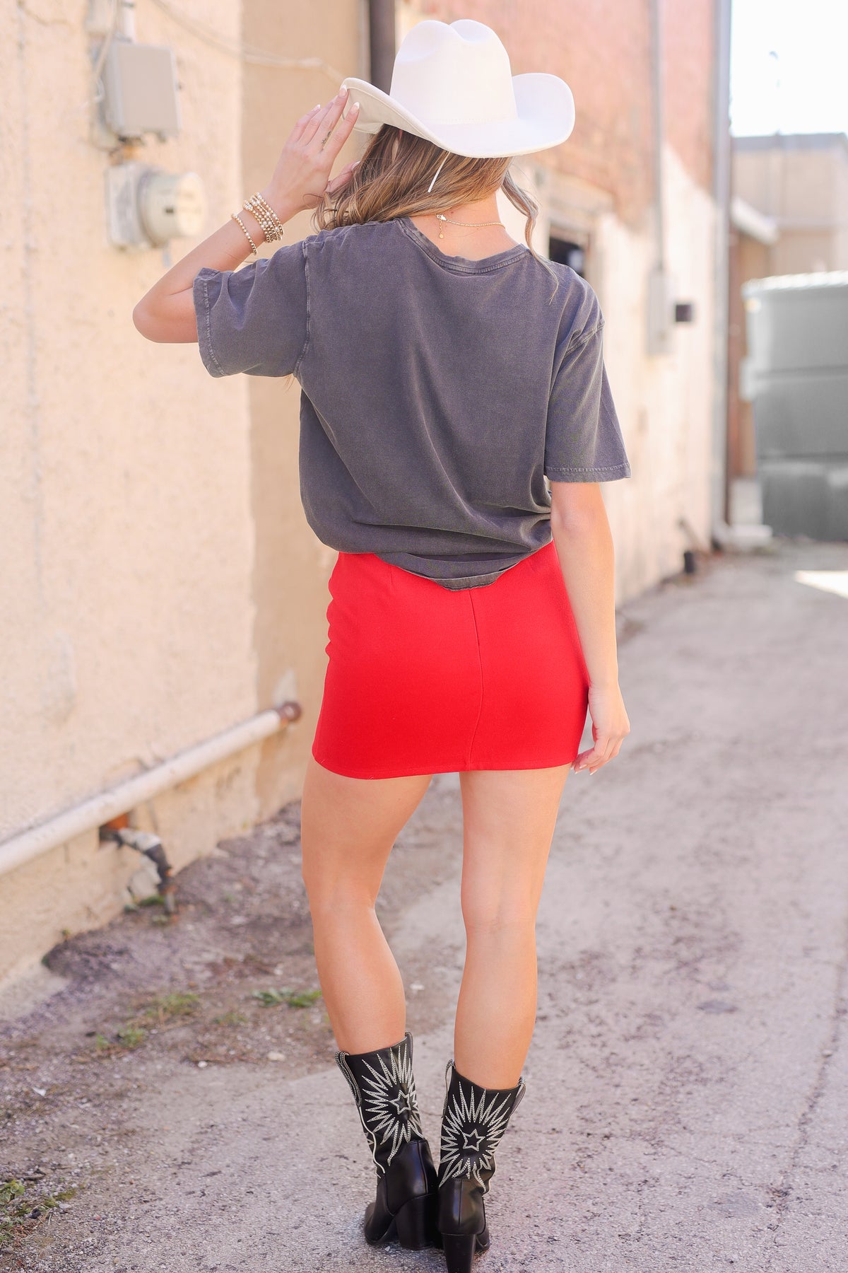 Person wearing a gray shirt, red skirt, and cowboy hat walking on a sidewalk.