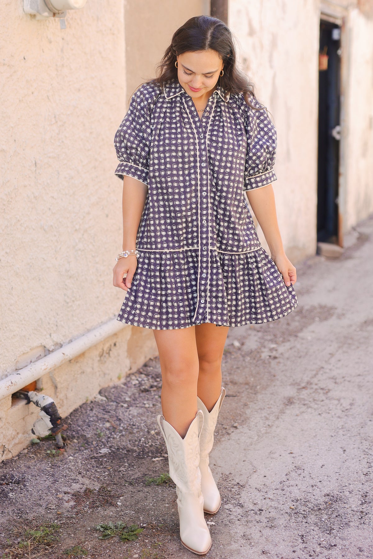 Woman wearing a checkered dress and white cowboy boots on a street.