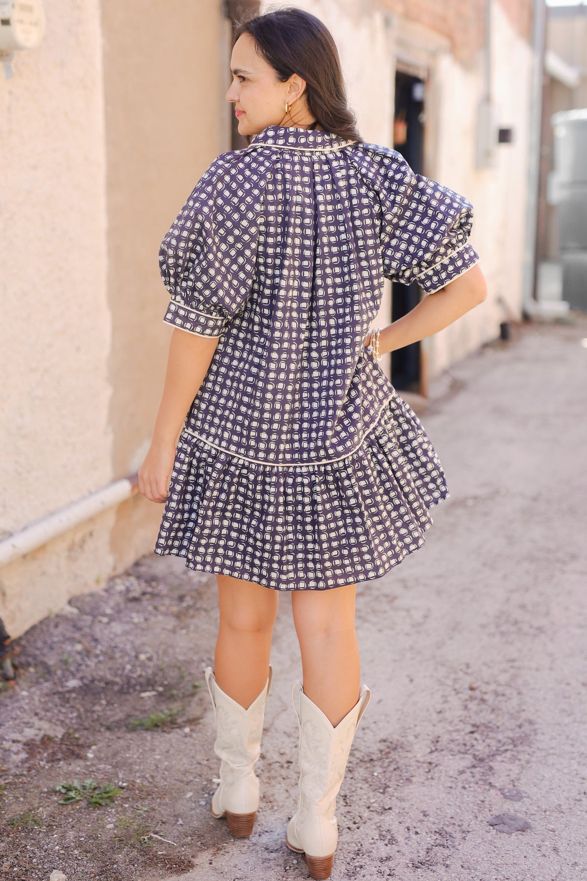 Woman in a checkered dress and white cowboy boots walking down a street.