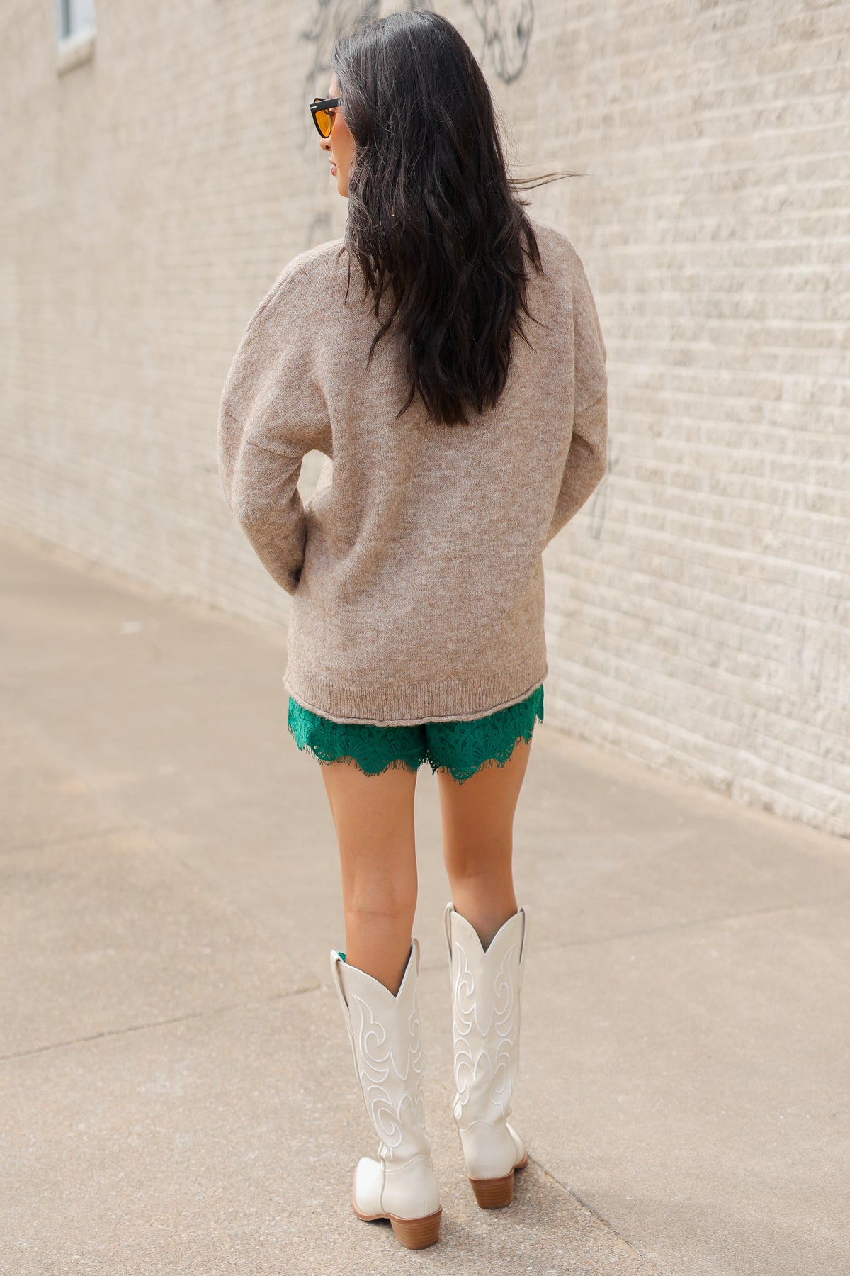 Brunette model wearing a mallard print knit sweater and green lace shorts with white cowboy boots standing outside. Southern House Clothing