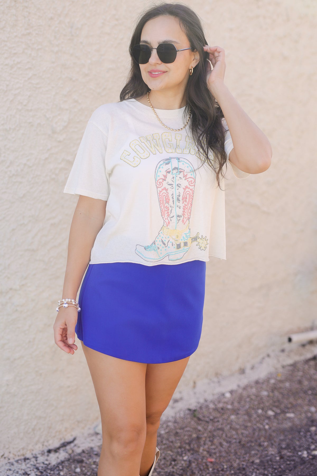 Woman wearing a graphic t-shirt and blue skirt against a beige wall.