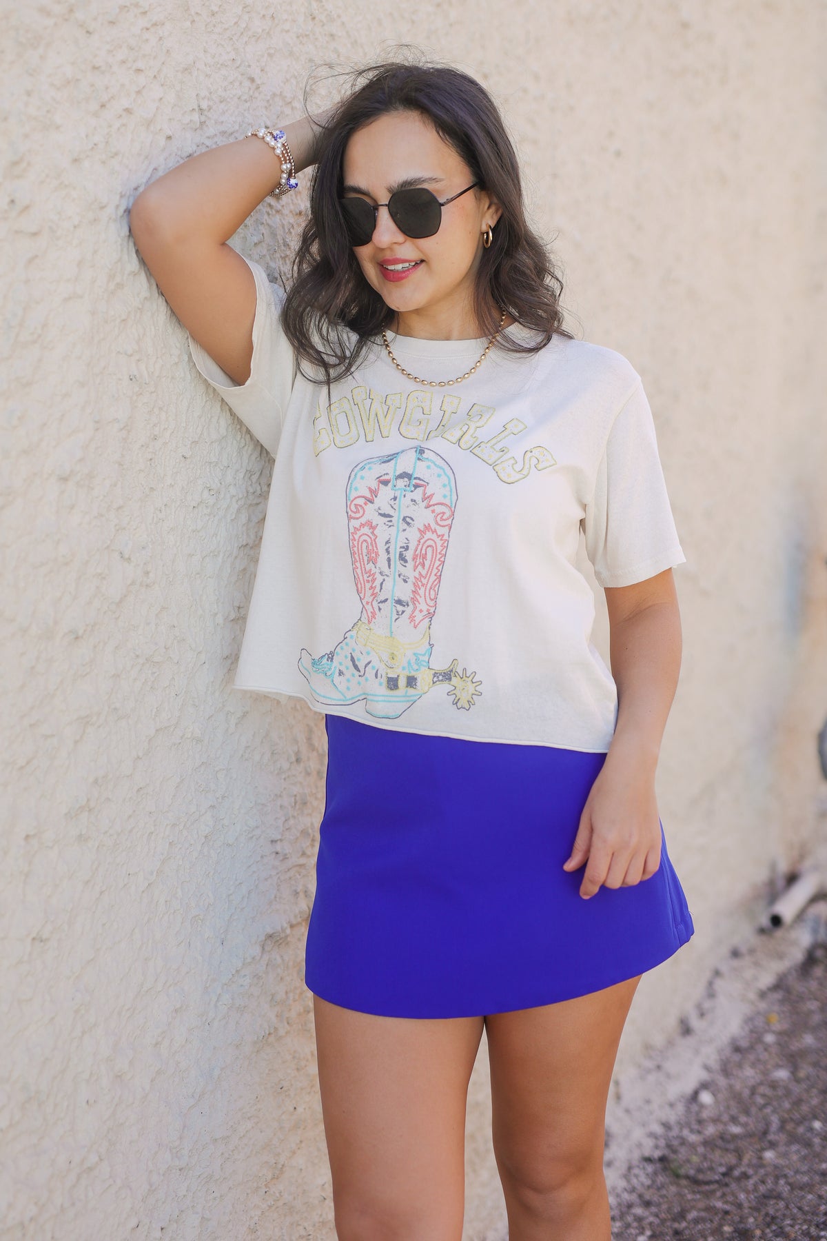 Woman wearing a graphic t-shirt and blue skirt against a beige wall.
