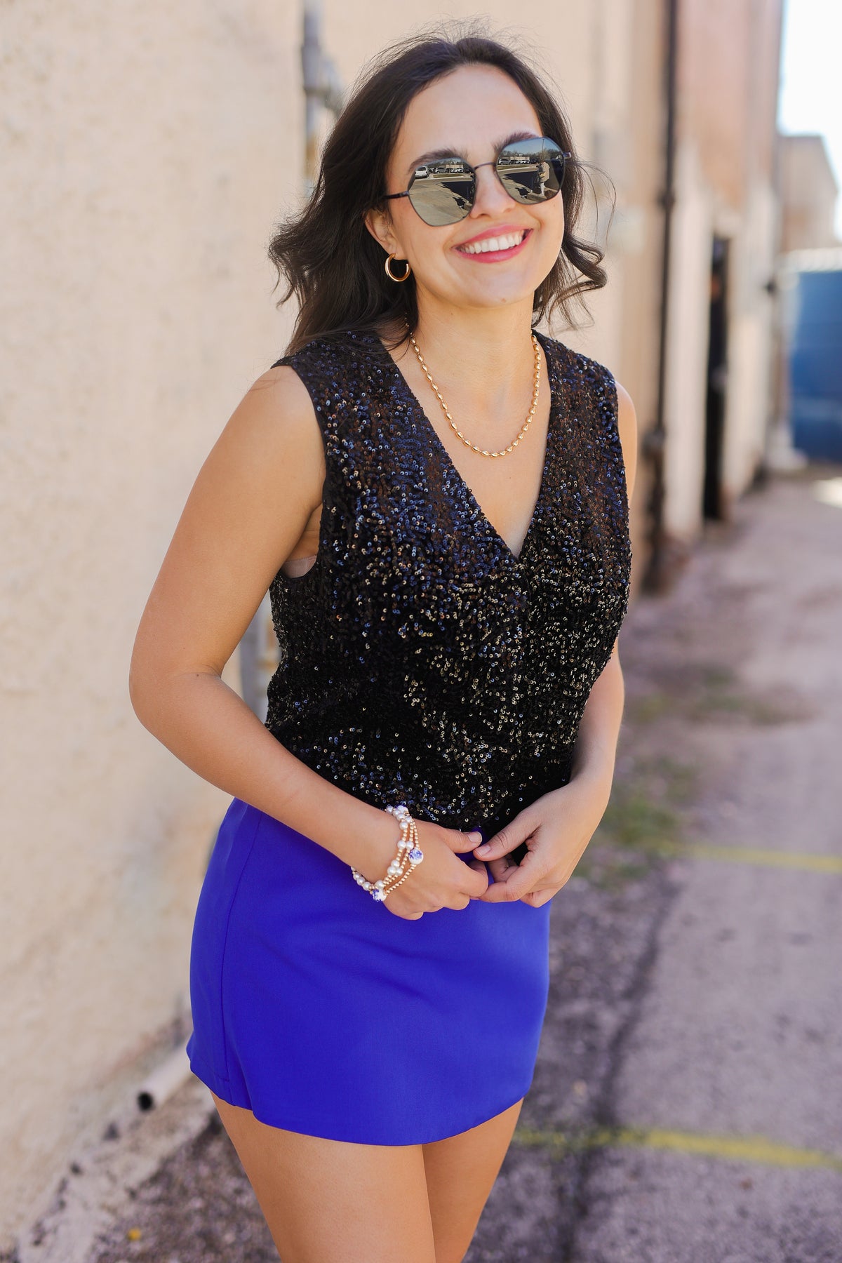 Woman wearing a black sequin top and blue skirt standing against a beige wall.