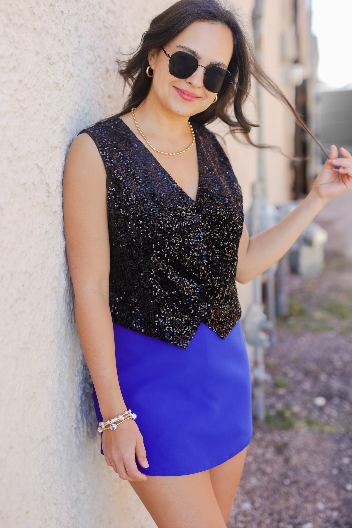 Woman wearing a black sequin top and blue skirt against a textured wall.