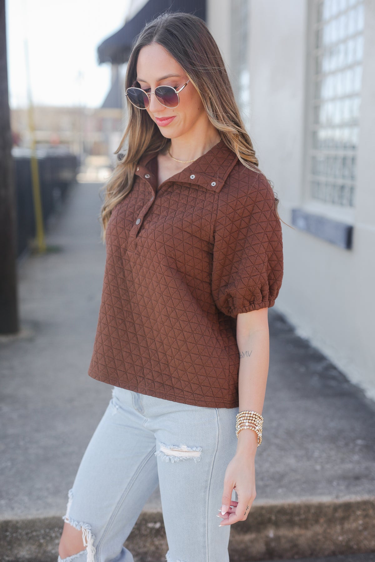 Woman wearing a brown quilted top and light jeans outdoors.