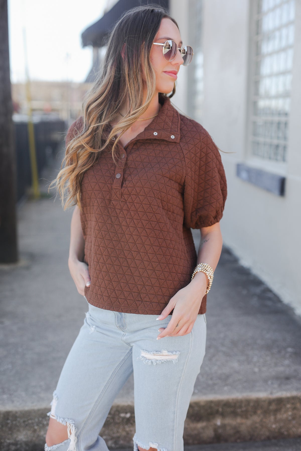 Woman wearing a brown textured shirt and light blue jeans outdoors.