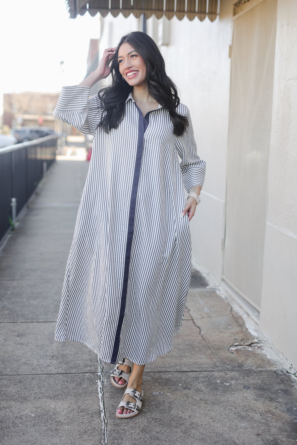 Woman wearing a long striped shirt dress on a sidewalk.