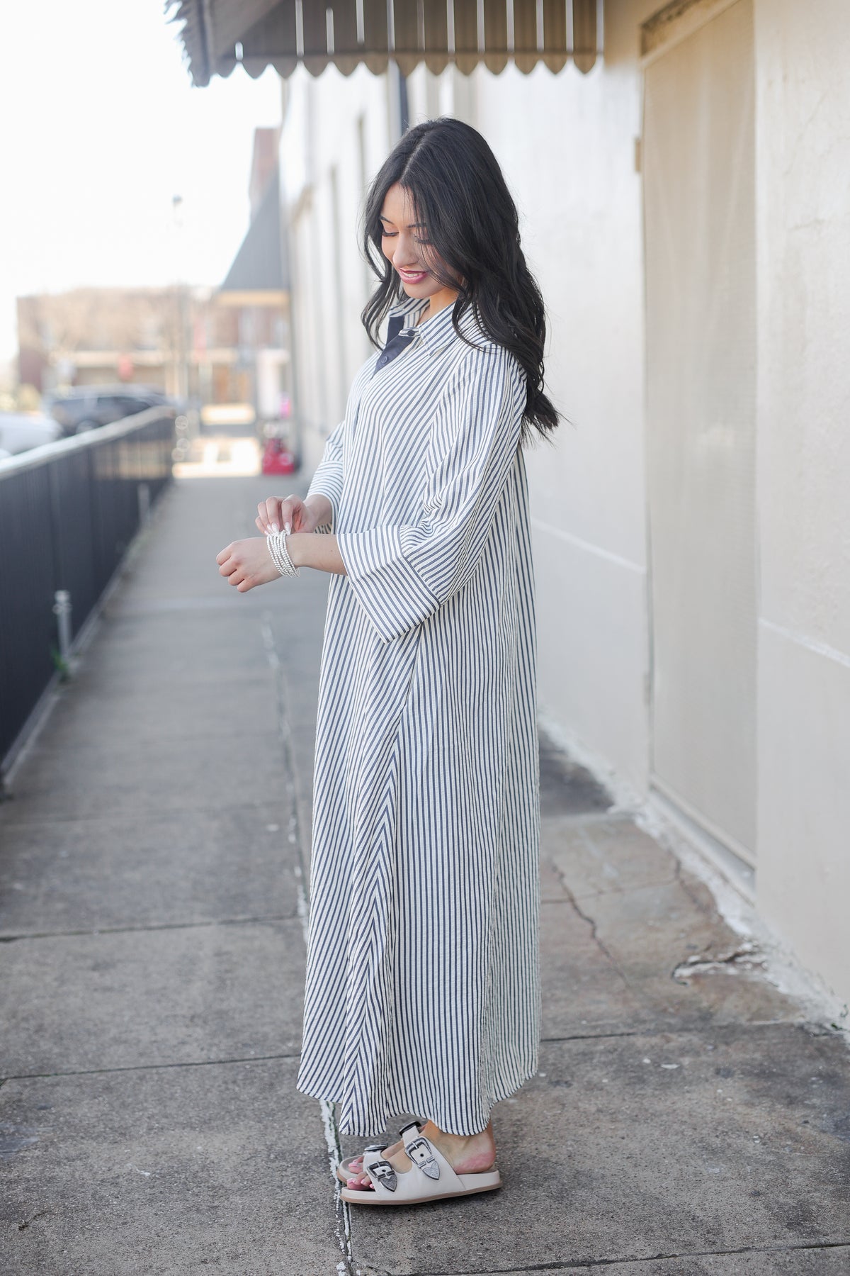 Woman in a long, light-colored dress standing on a sidewalk.