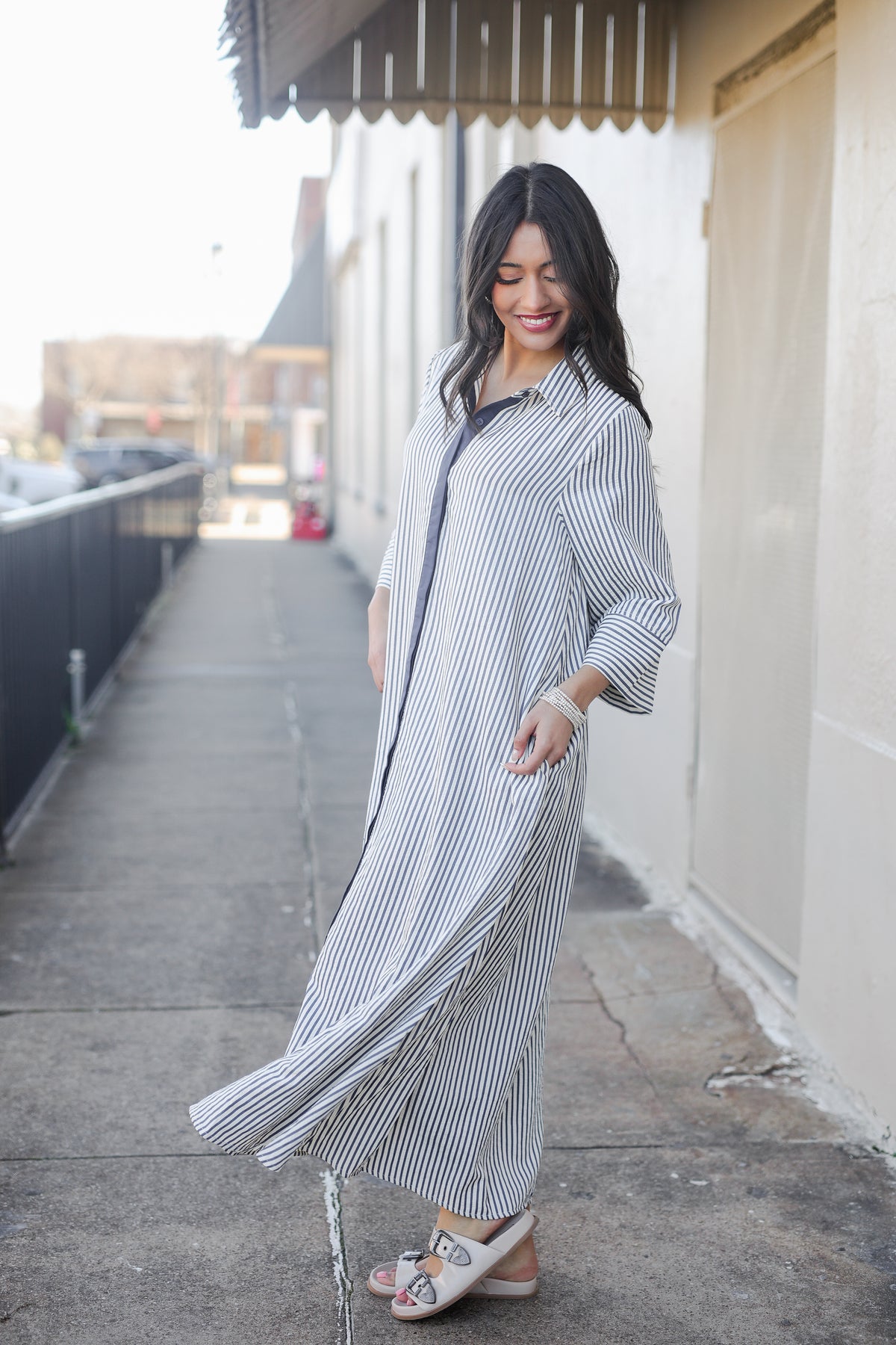Woman wearing a long, light-colored striped dress on a city street.