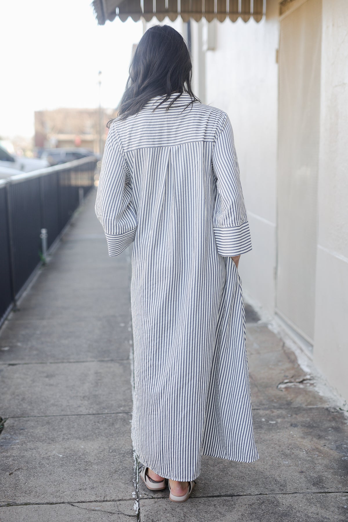 Person wearing a long, striped shirt dress on a sidewalk.