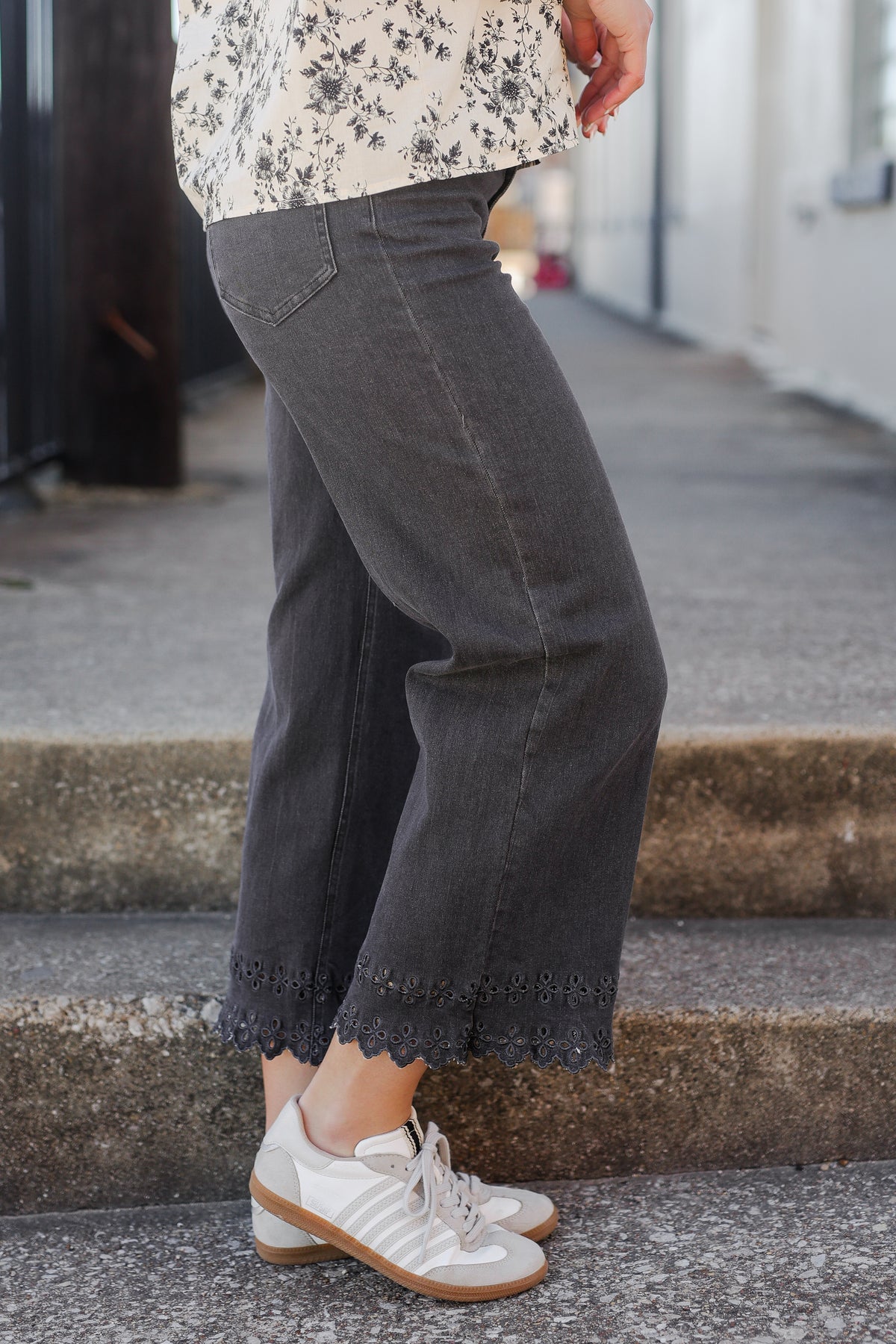 Person wearing dark gray pants and white sneakers on a sidewalk.