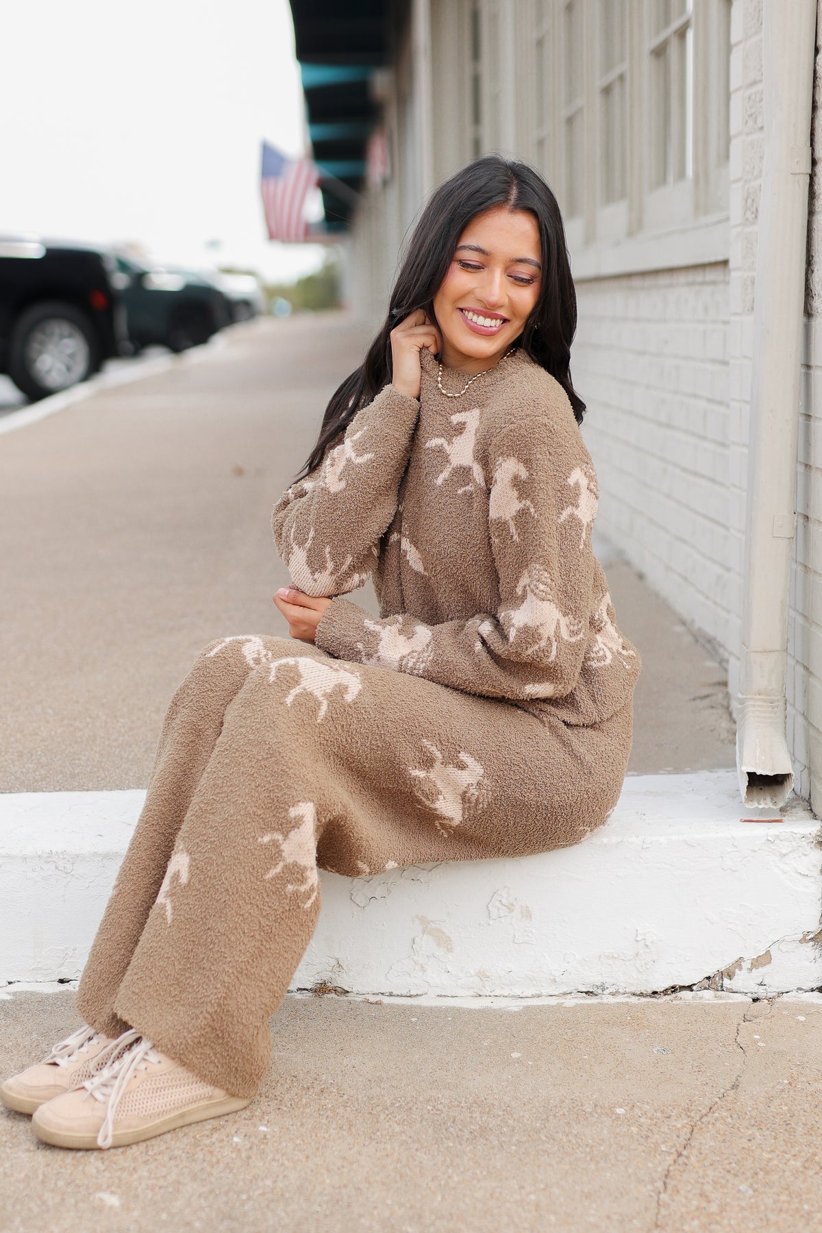 Brunette model wearing Bridlebrook Running Horse Sweater in Mocha featuring a fuzzy textured knit, cream running horse pattern, crew neckline, and long sleeves. it is paired with the Bridlebrook Running Horse Pants with the same pattern to make a set. Southern House Clothing